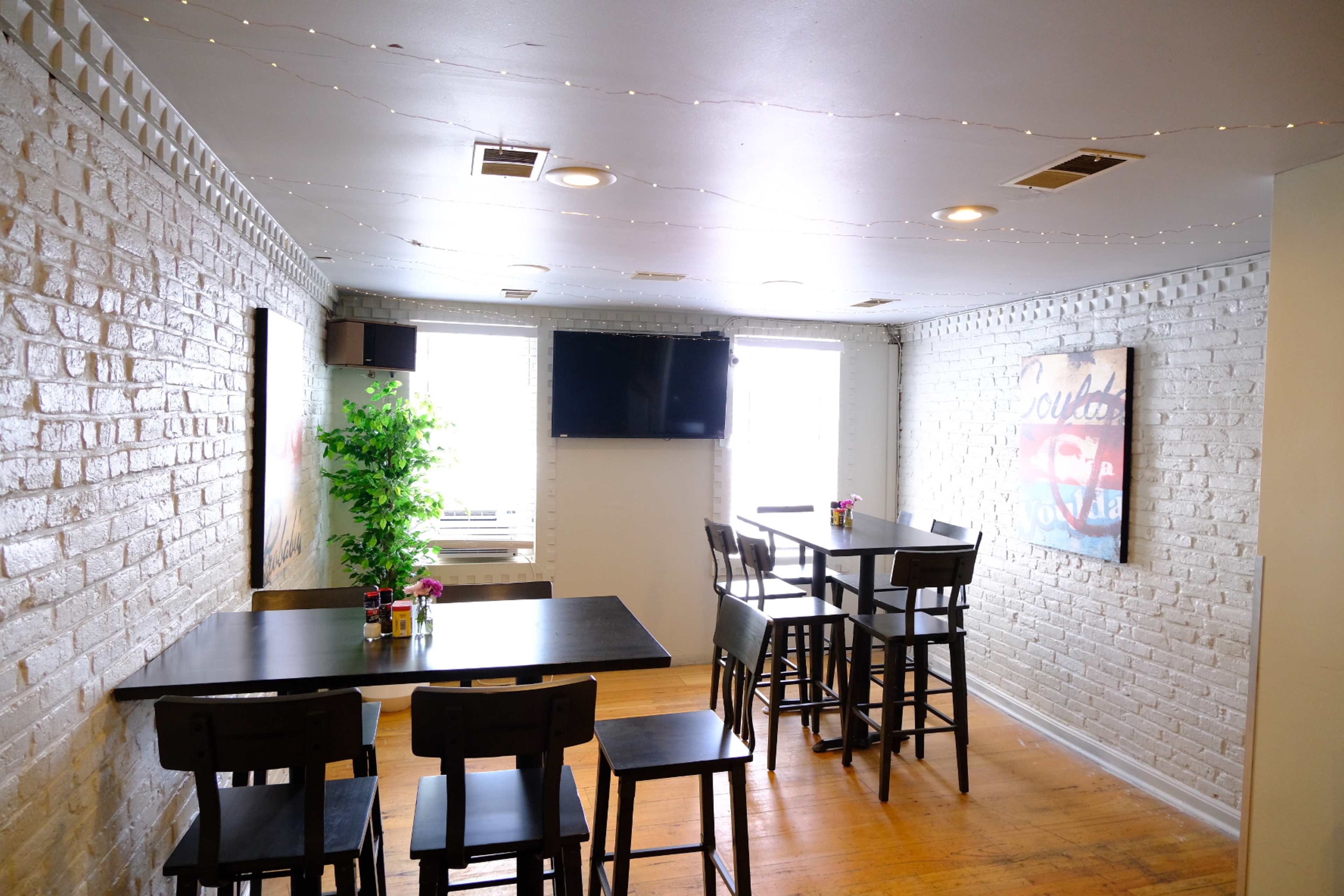 A dining area with wooden tables and chairs, white brick walls, and bright overhead lighting.
