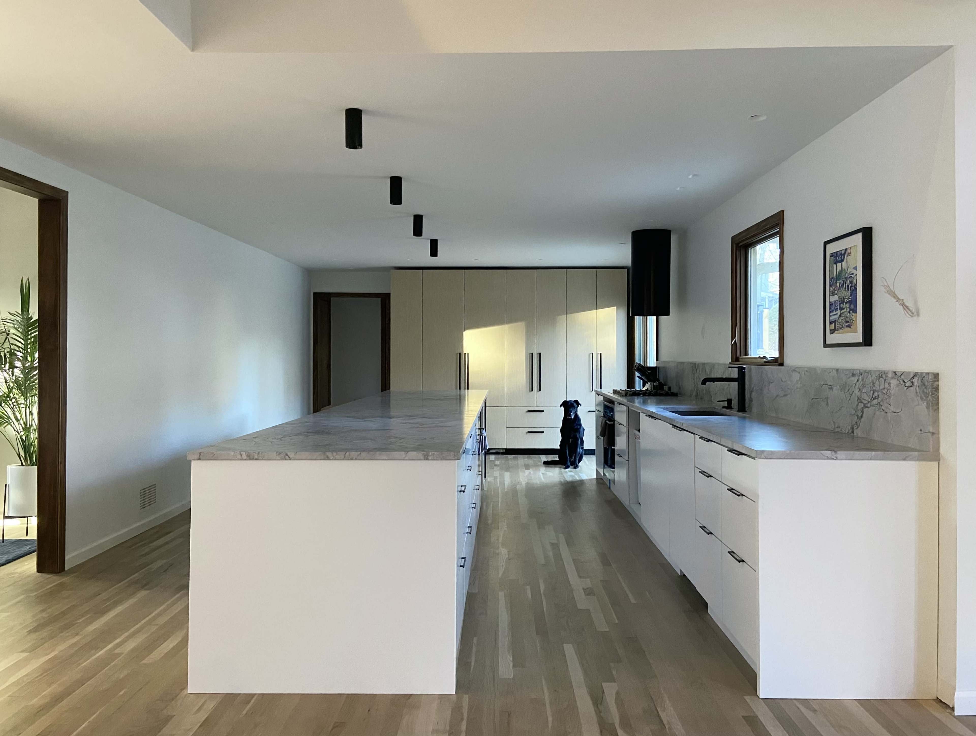 A spacious modern kitchen features a large island with marble countertops and sleek cabinetry, illuminated by black pendant lights.