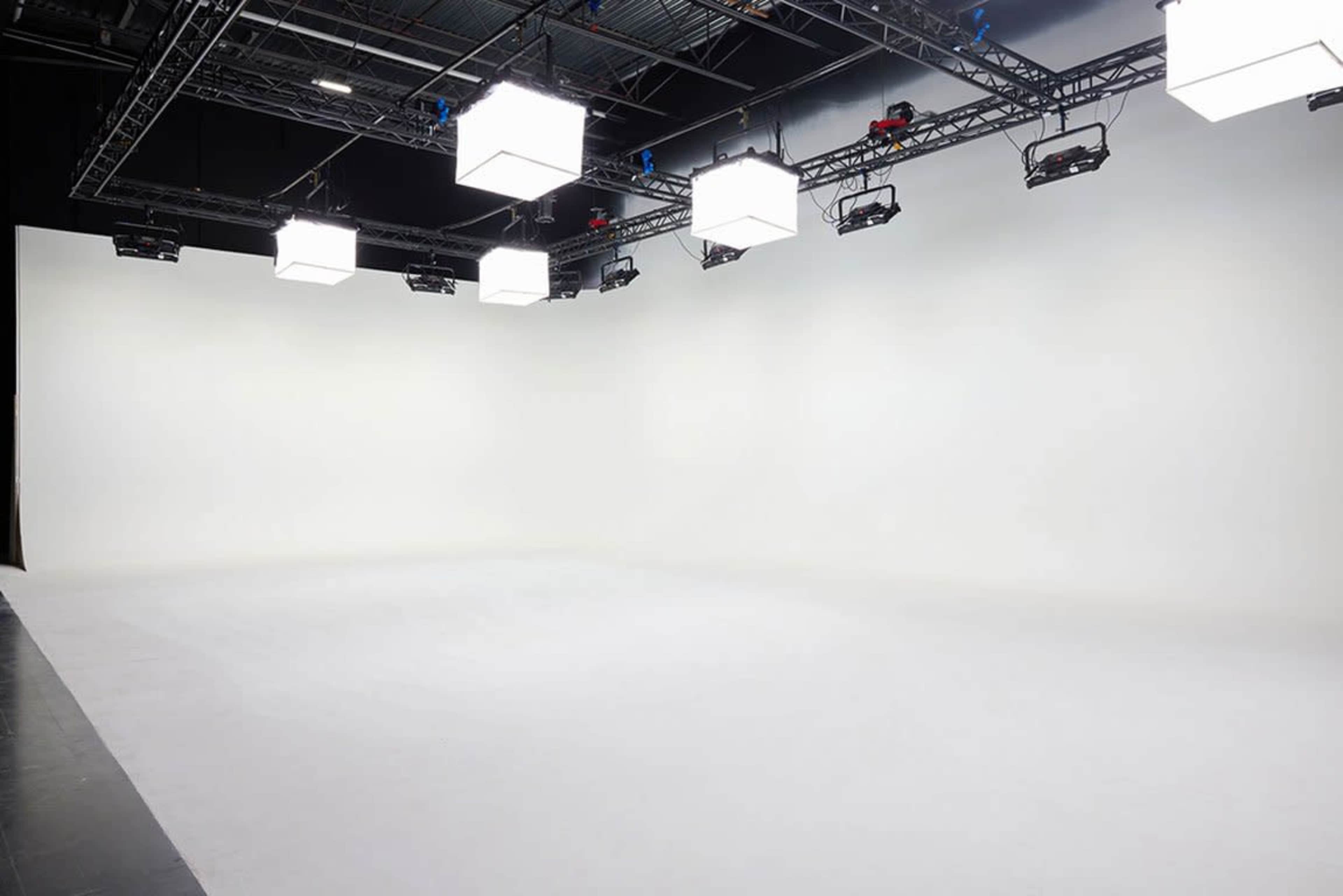 A spacious, well-lit studio interior with a plain white backdrop and ceiling-mounted lighting fixtures.