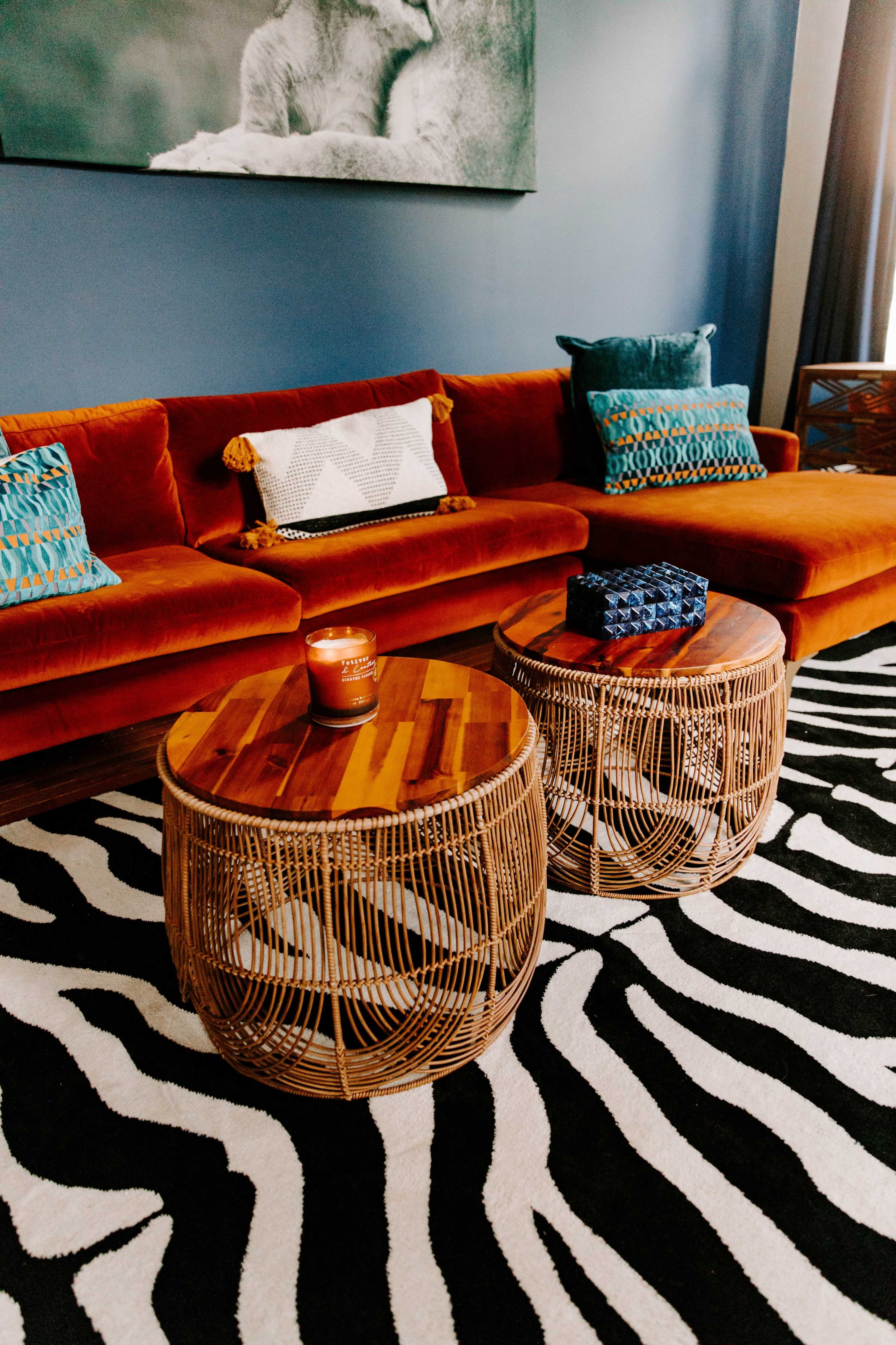 A living room with an orange sofa adorned with textured pillows, two round wooden coffee tables, and a black-and-white zebra-striped rug.