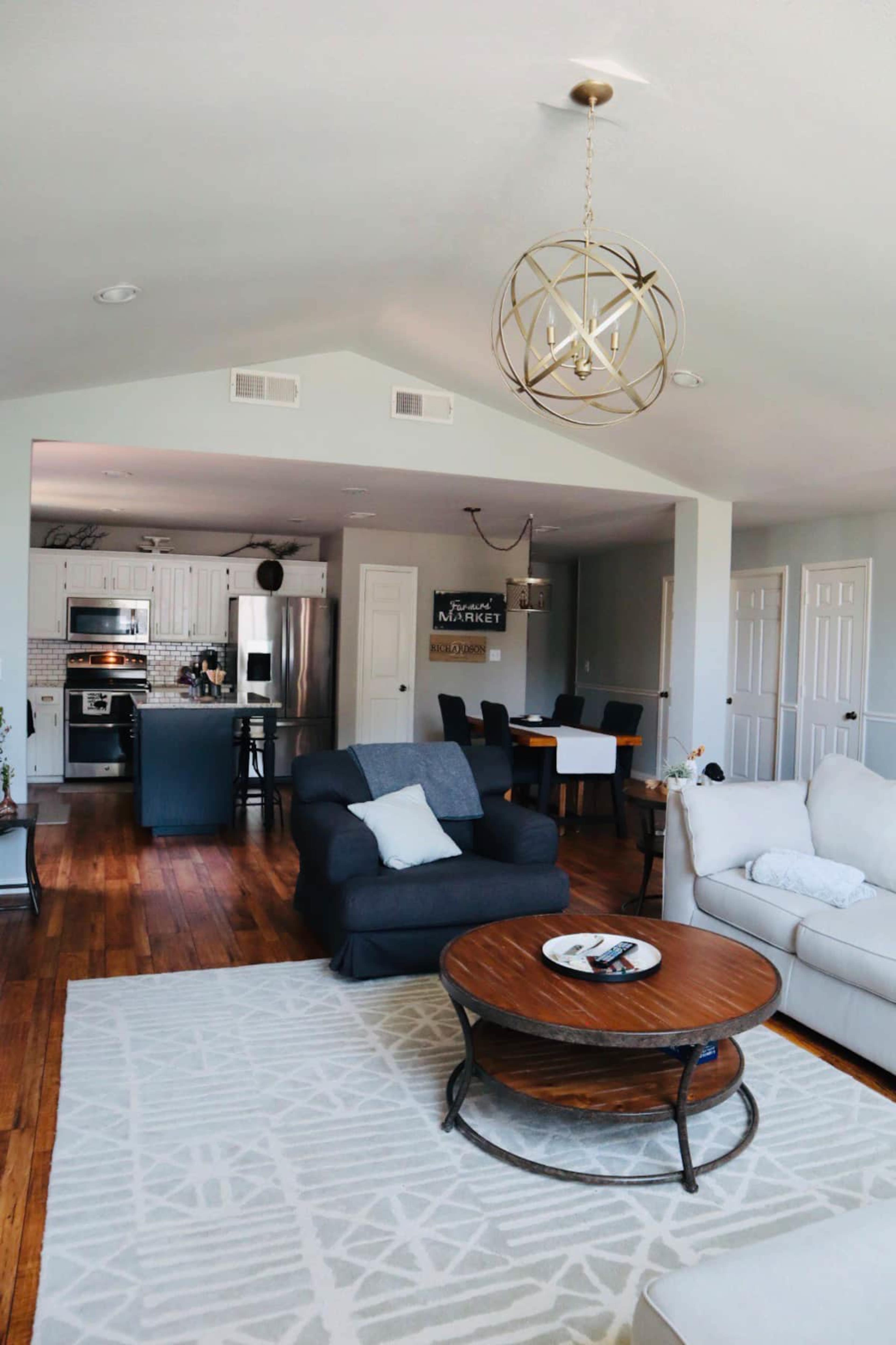 A spacious living area with a dark sofa, a round coffee table, and an open layout connecting to a kitchen and dining area.