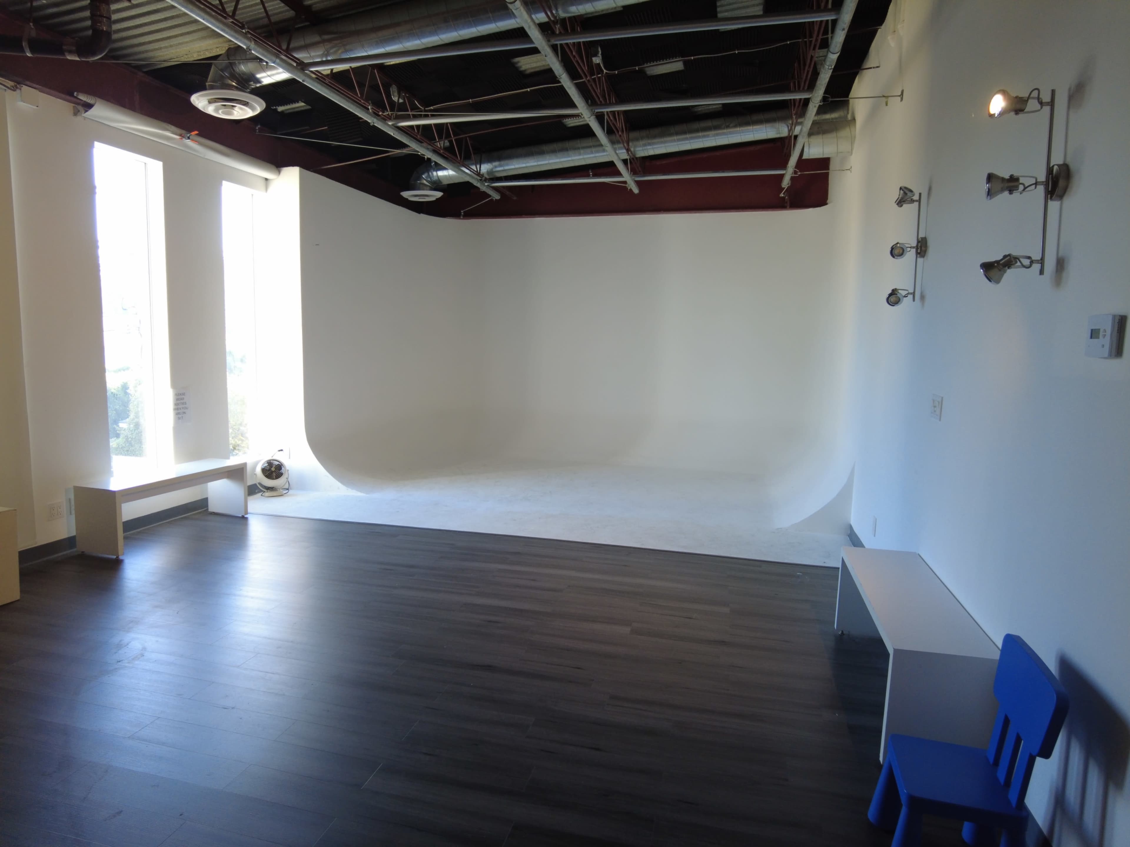 The image shows a spacious studio with a white backdrop, wooden flooring, and large windows allowing natural light to enter.
