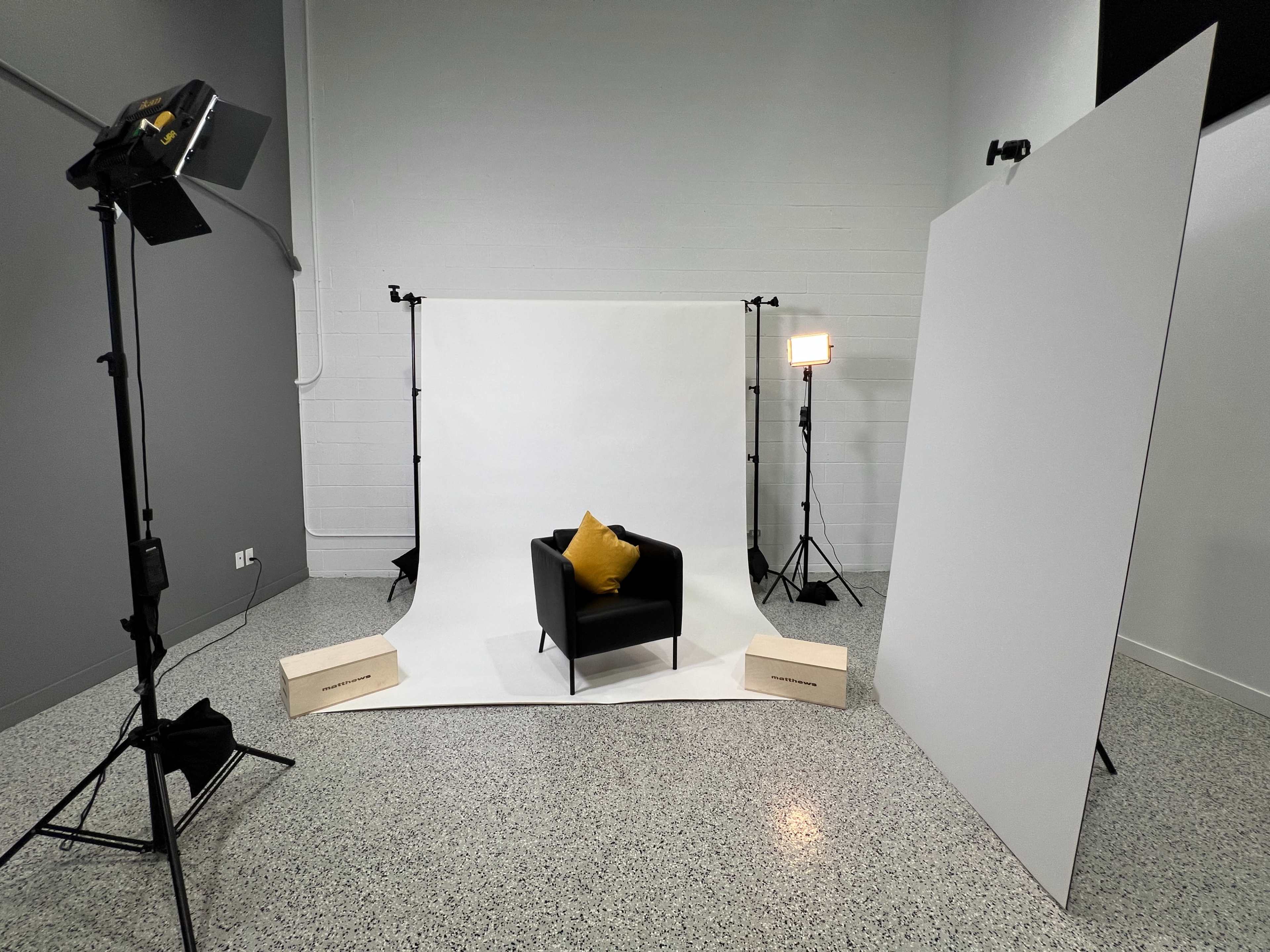 A photography setup featuring a black armchair with a yellow cushion in front of a white backdrop, illuminated by lights on either side.