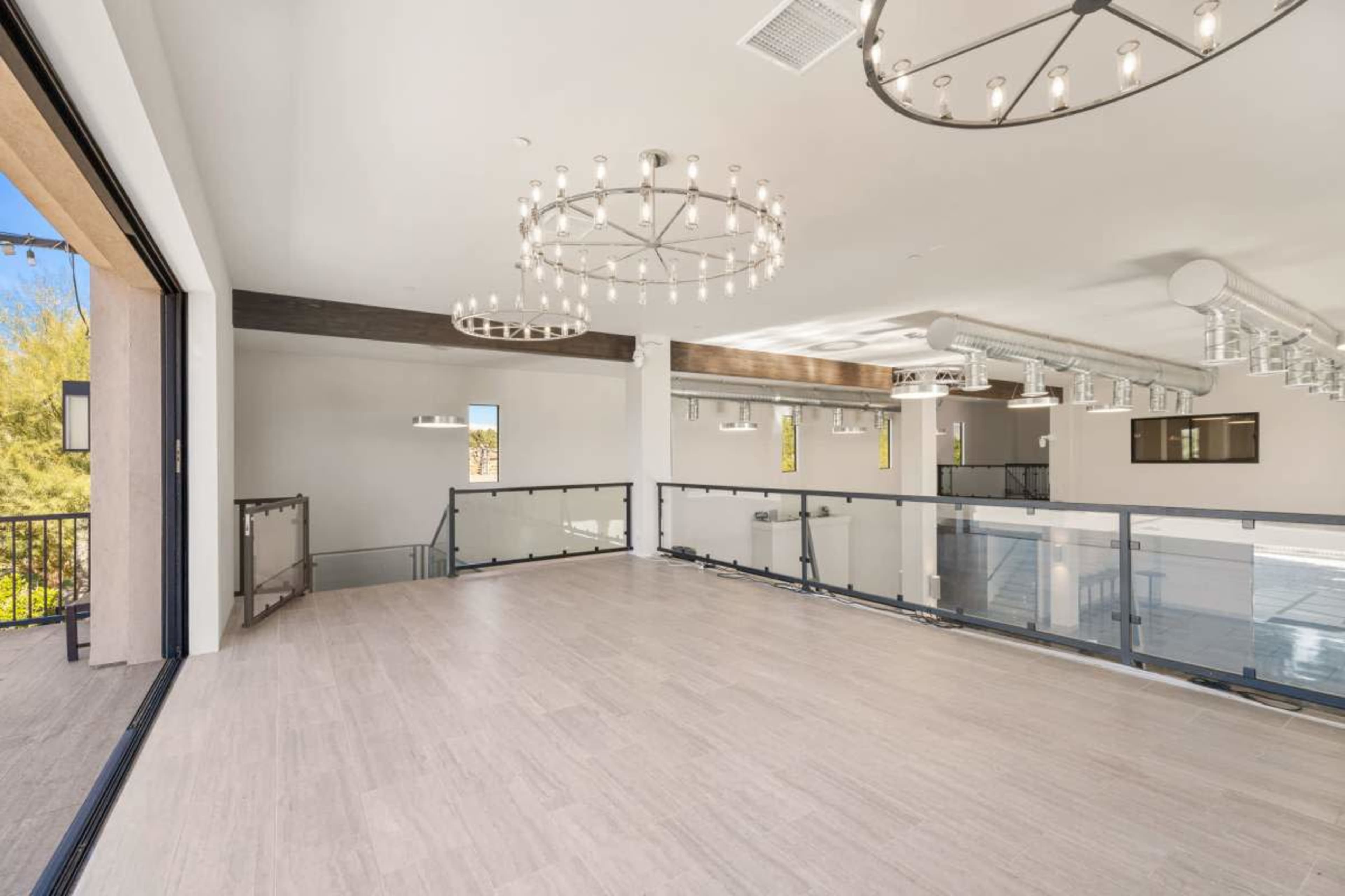 The image shows a spacious, well-lit interior with large windows, modern chandeliers, and a balcony overlooking the lower level.