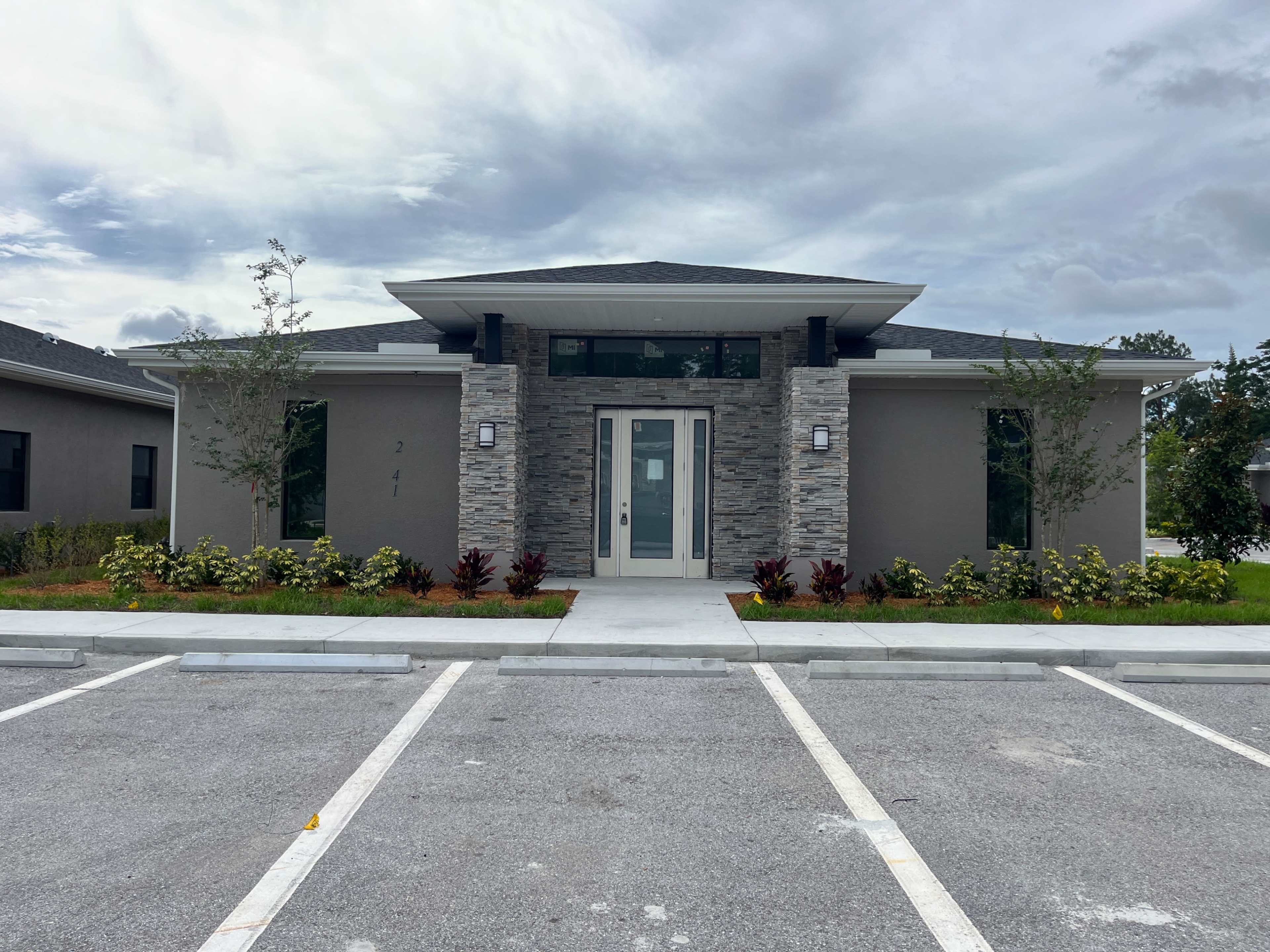 A modern single-story building with a stone and stucco facade, flanked by landscaped areas and a parking lot in front.