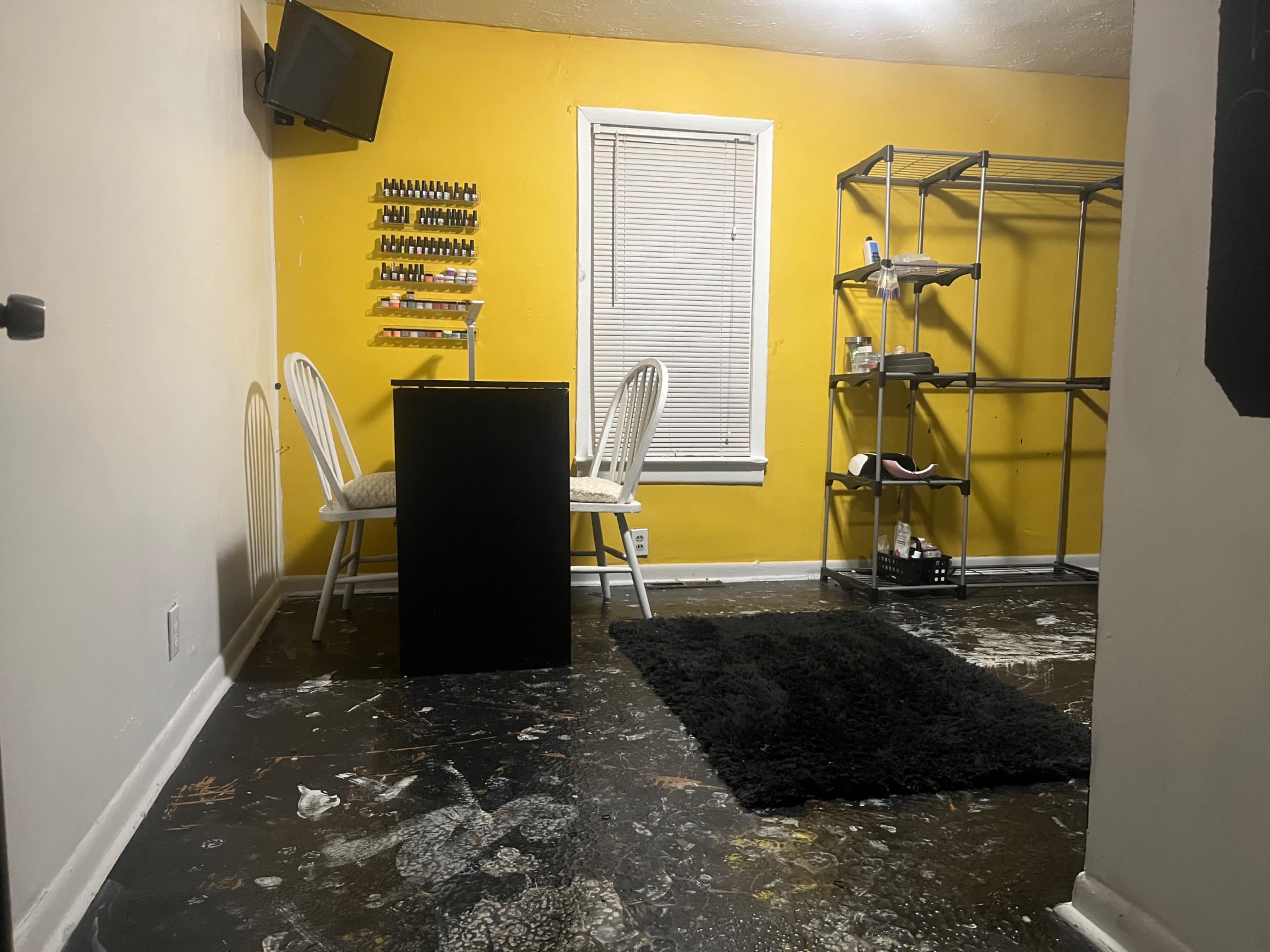 A small room with a yellow wall, two chairs at a black table, and a shelving unit near a window.