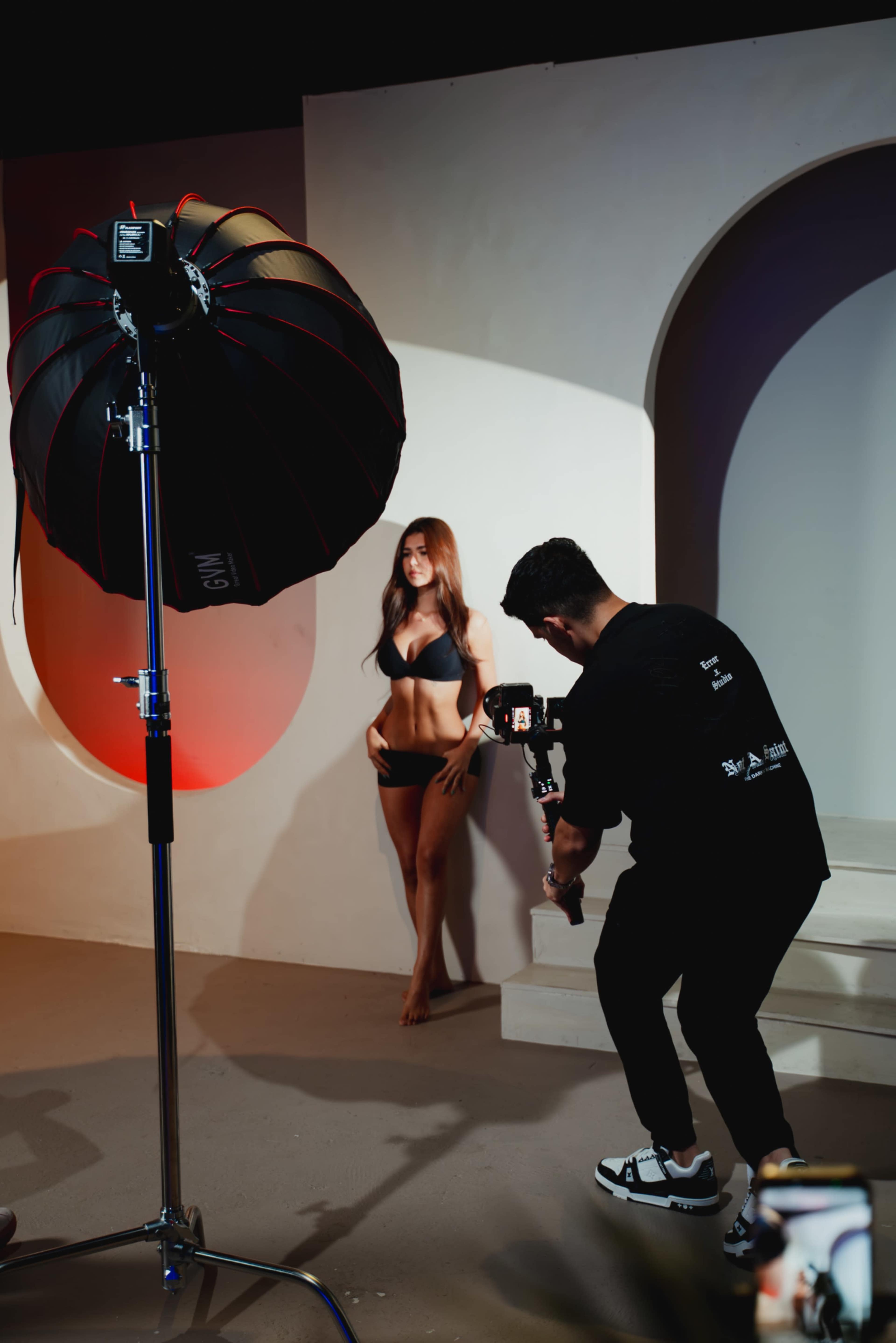 A photographer captures a model posing in a bikini under studio lighting.