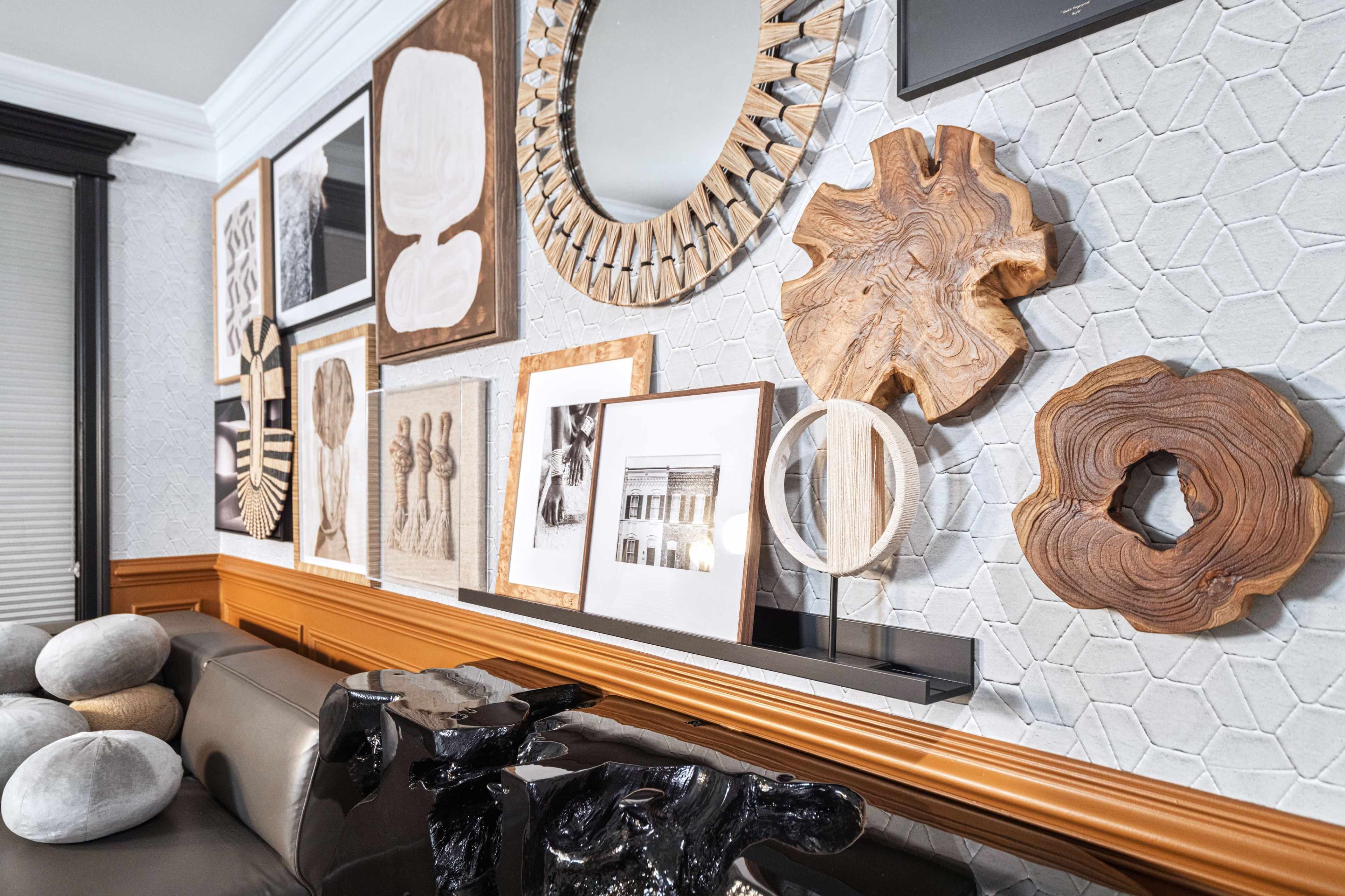 A modern interior wall adorned with various art pieces, including wooden sculptures and framed photographs, above a dark-colored sofa.