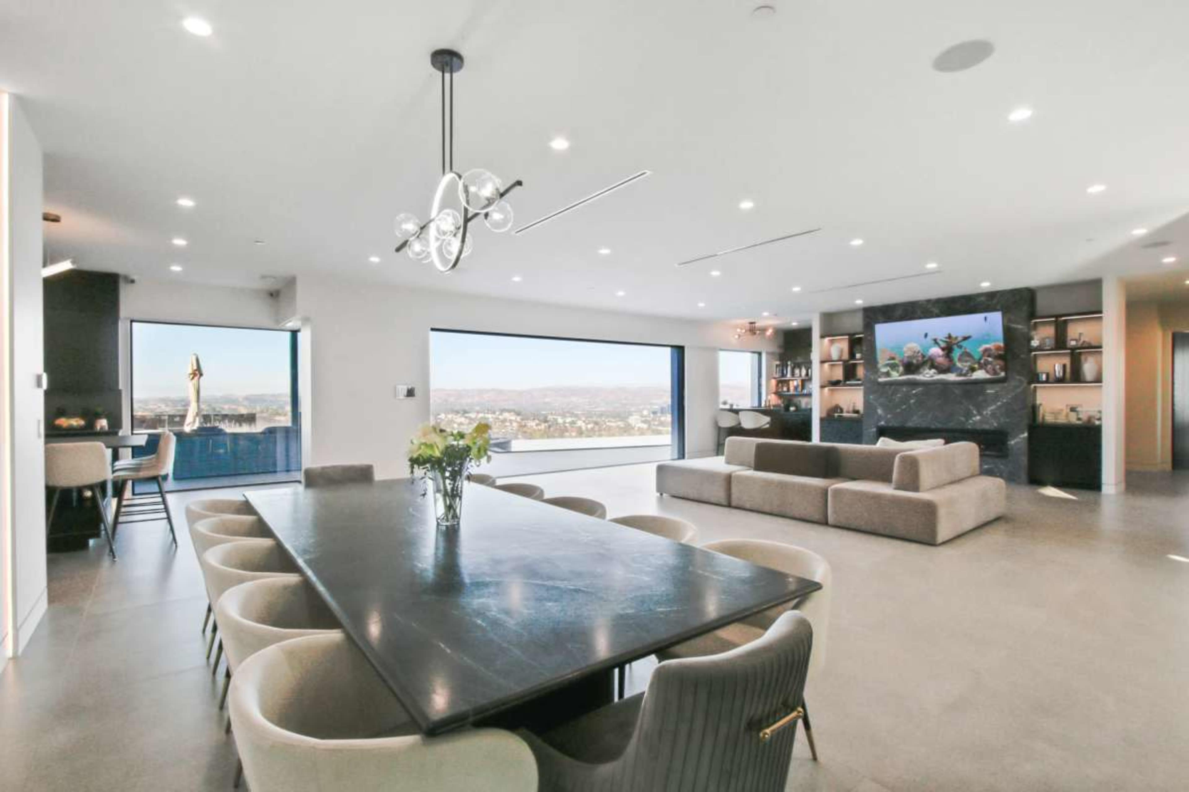 The image shows a modern open-concept living and dining area with large windows, a dining table, and a sectional sofa.