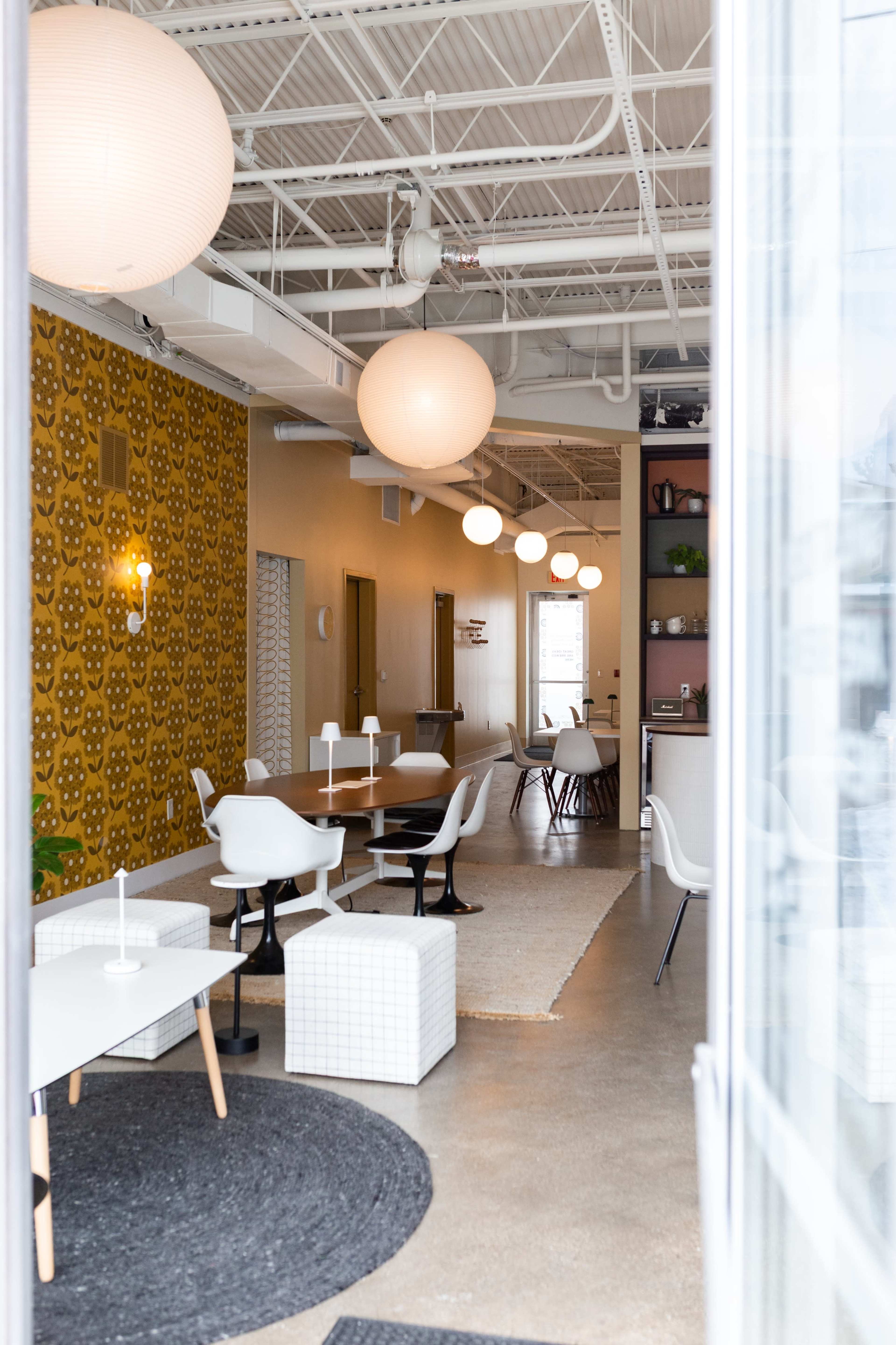 The image shows a modern interior space with multiple tables and chairs, a decorative wall with a floral pattern, and hanging light fixtures.