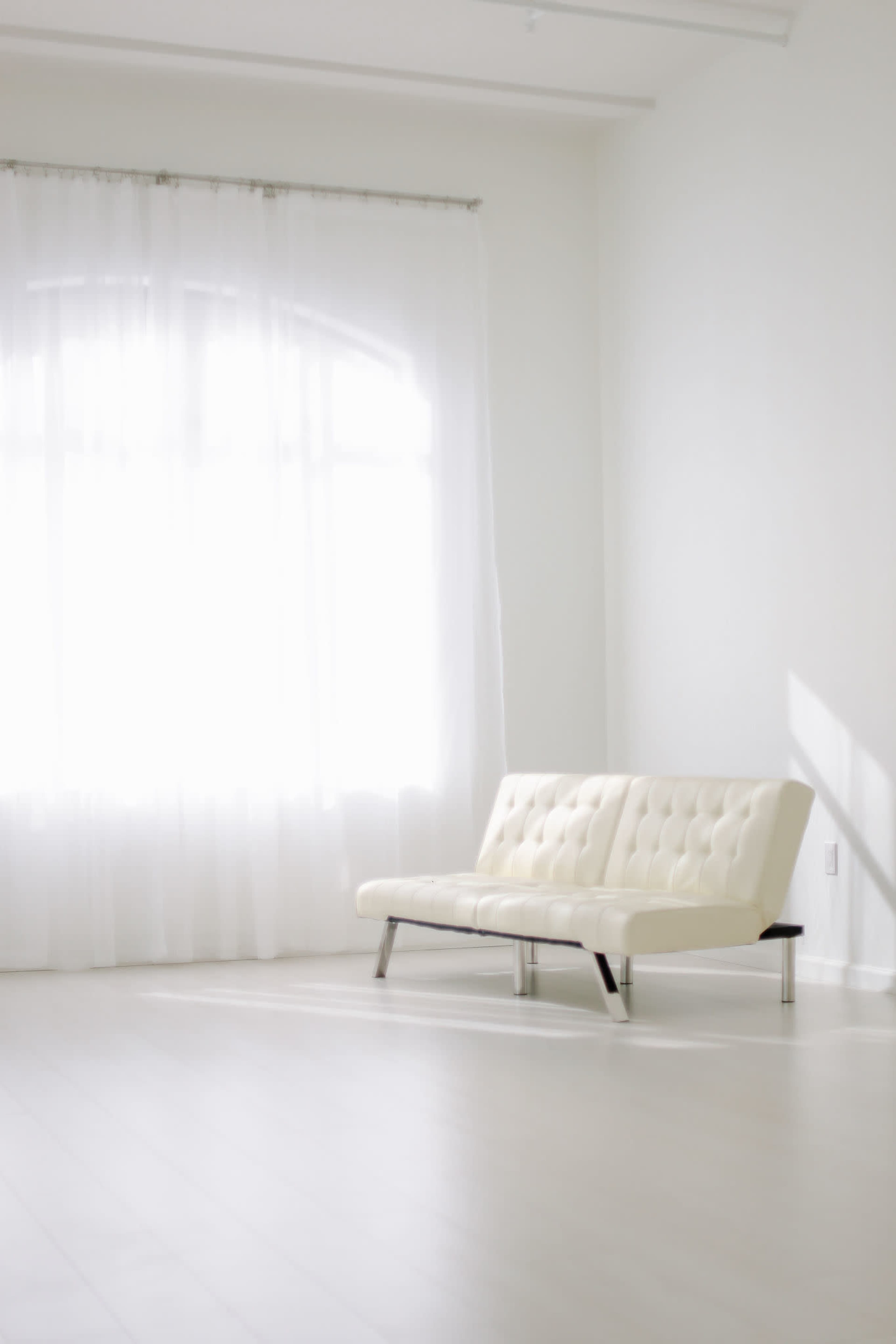 A white couch is positioned in a bright room with large windows and sheer curtains.