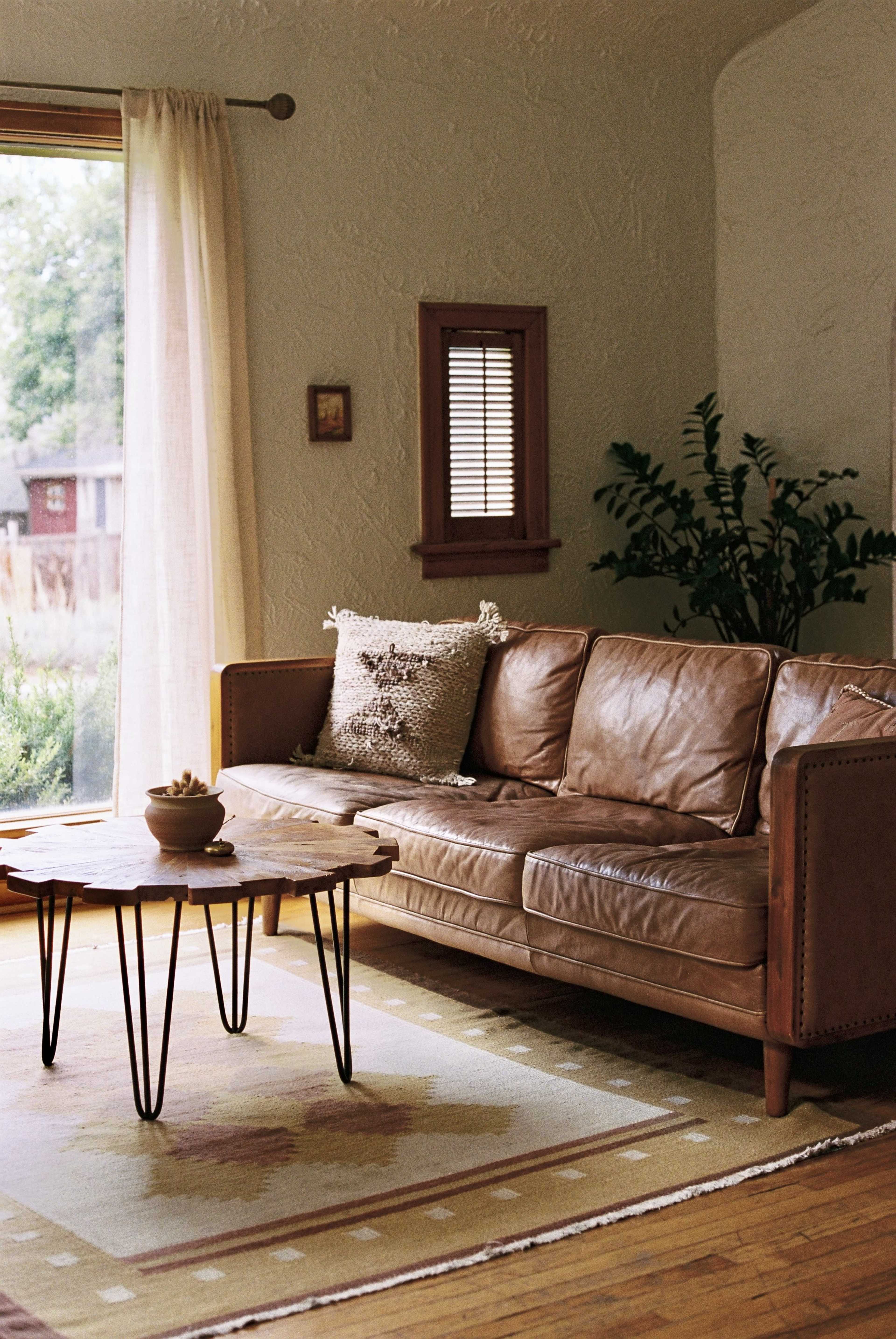 A leather couch is situated next to a wooden coffee table on a patterned rug in a well-lit living room.