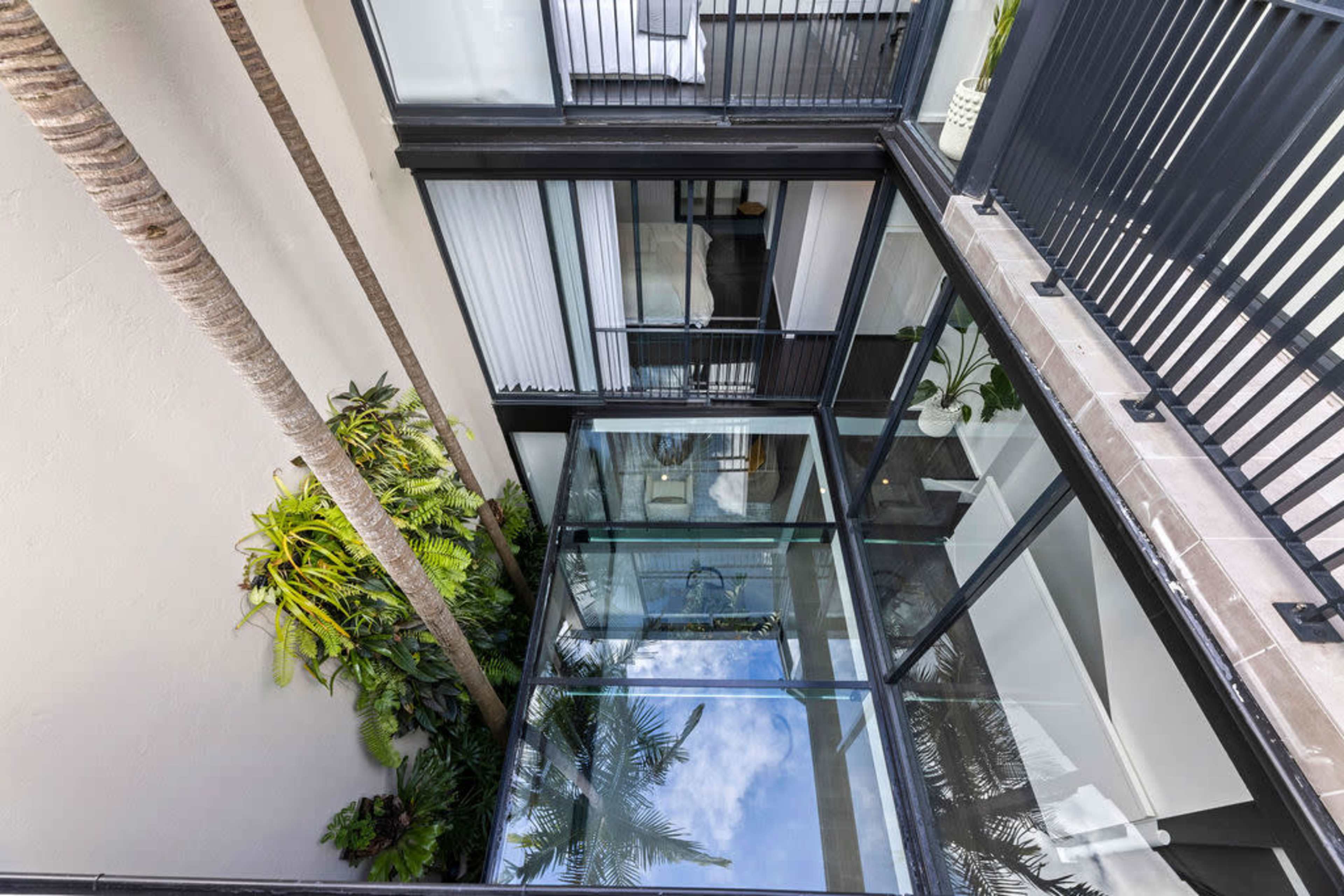An overhead view shows a glass-walled courtyard surrounded by modern buildings with palm trees and lush greenery.