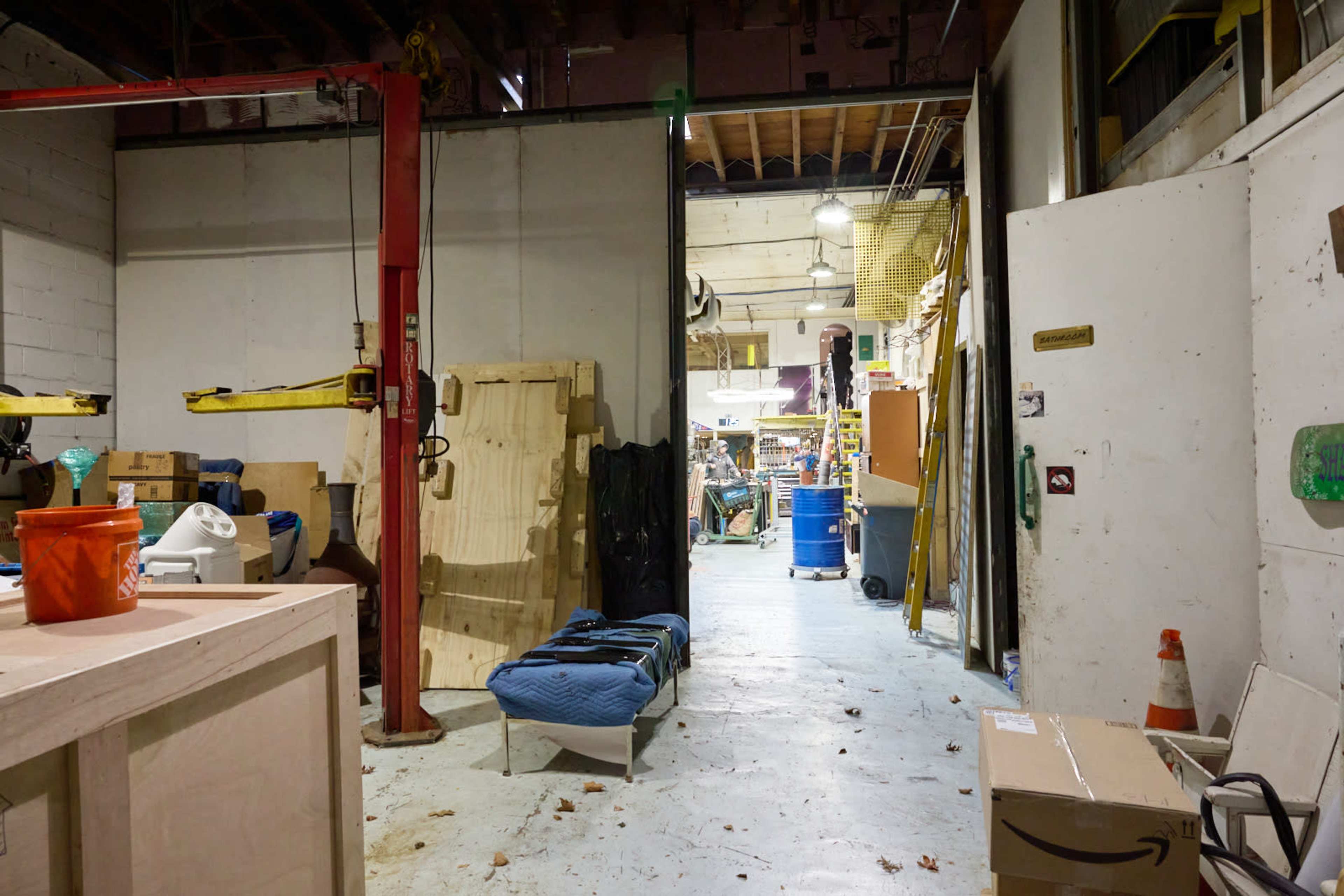 The image shows an industrial workspace with various tools, equipment, and materials stored along the walls and in the center of the room.