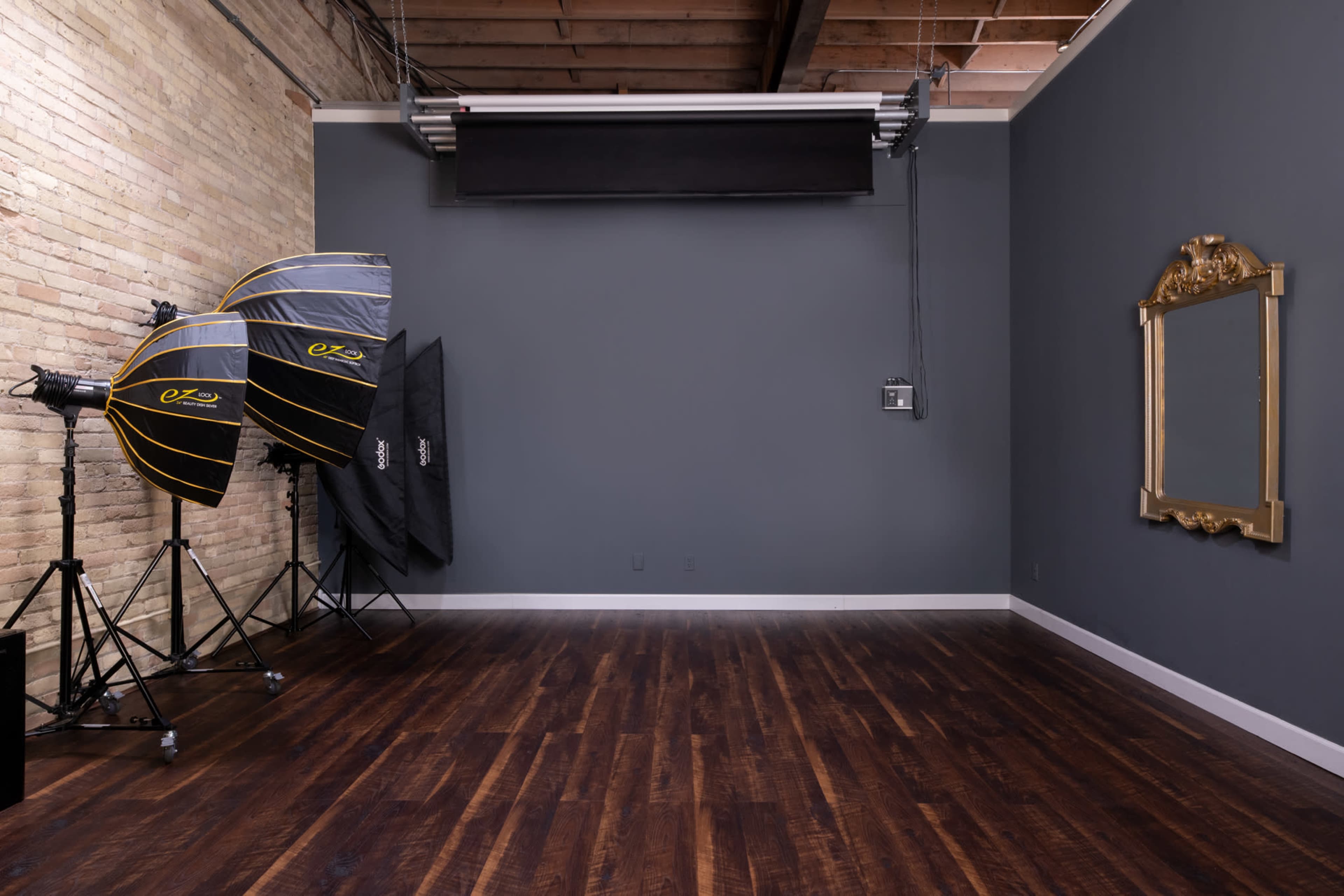 A spacious photography studio with two large softbox lighting setups and a vintage mirror mounted on a gray wall.
