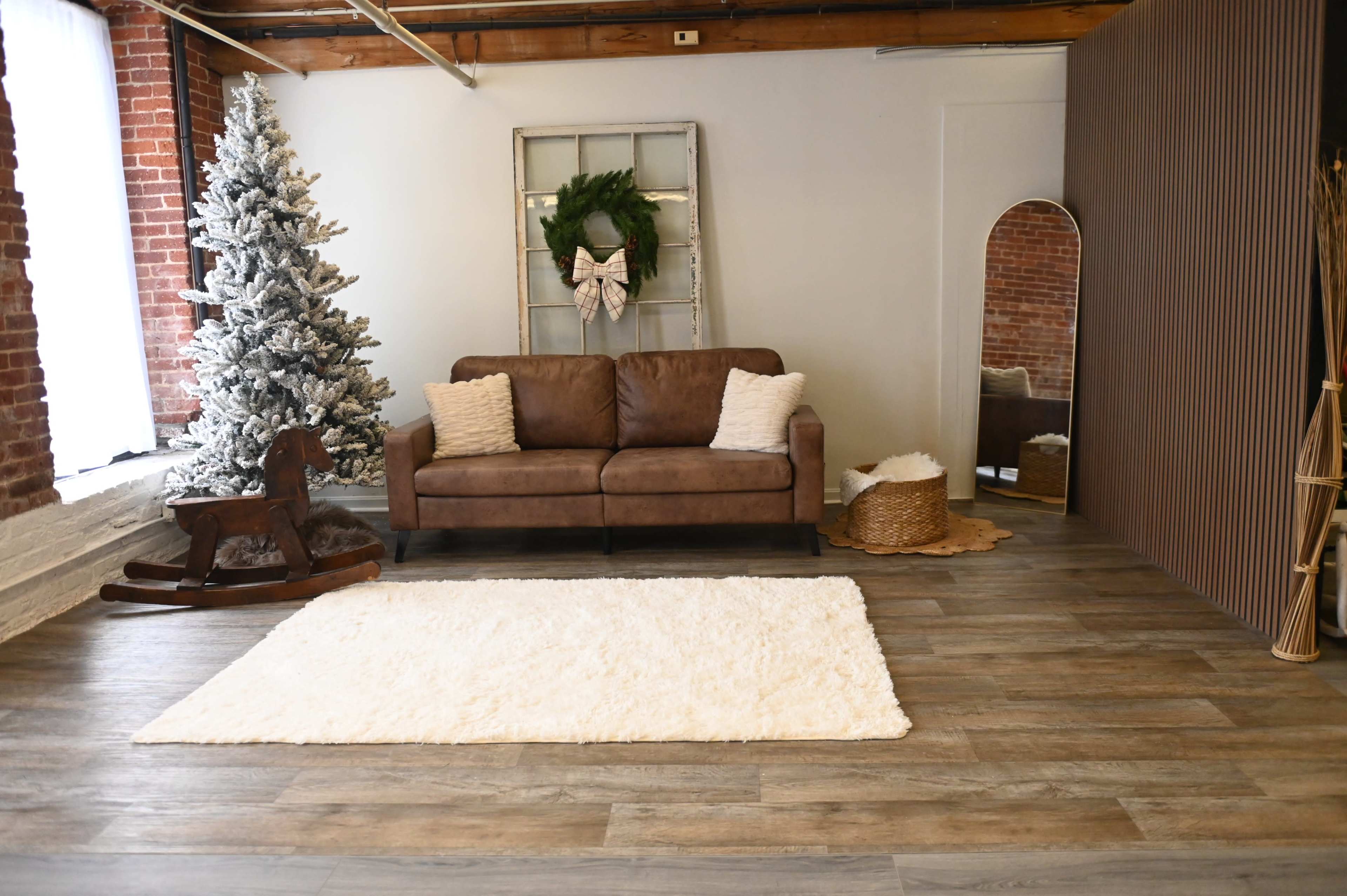 The scene shows a cozy interior featuring a brown sofa, a white rug on the floor, a Christmas tree, and decorative elements like a wreath and a mirror.