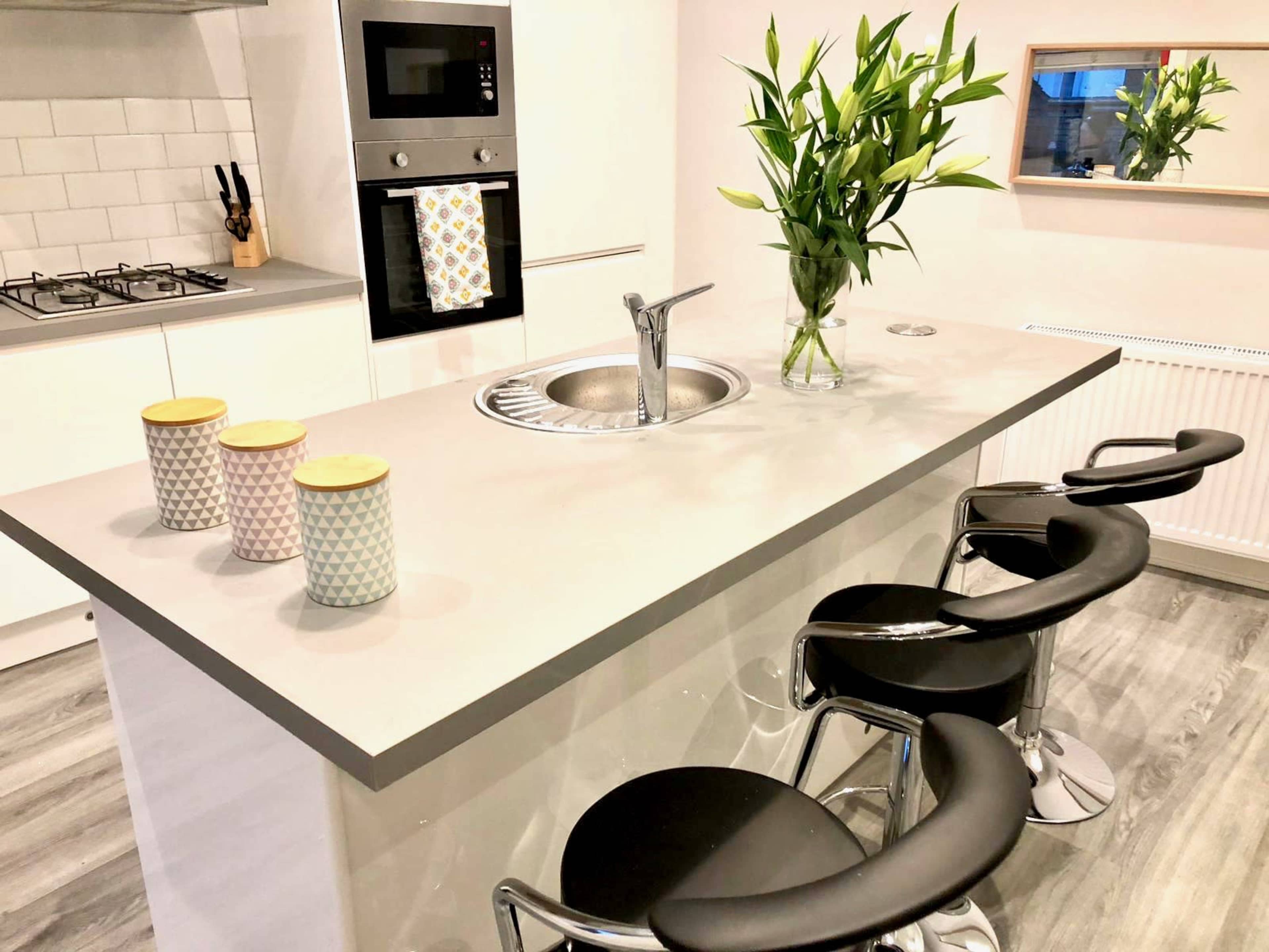 A modern kitchen features a central island with bar stools, a sink, and a vase of flowers, complemented by patterned canisters and sleek cabinetry.