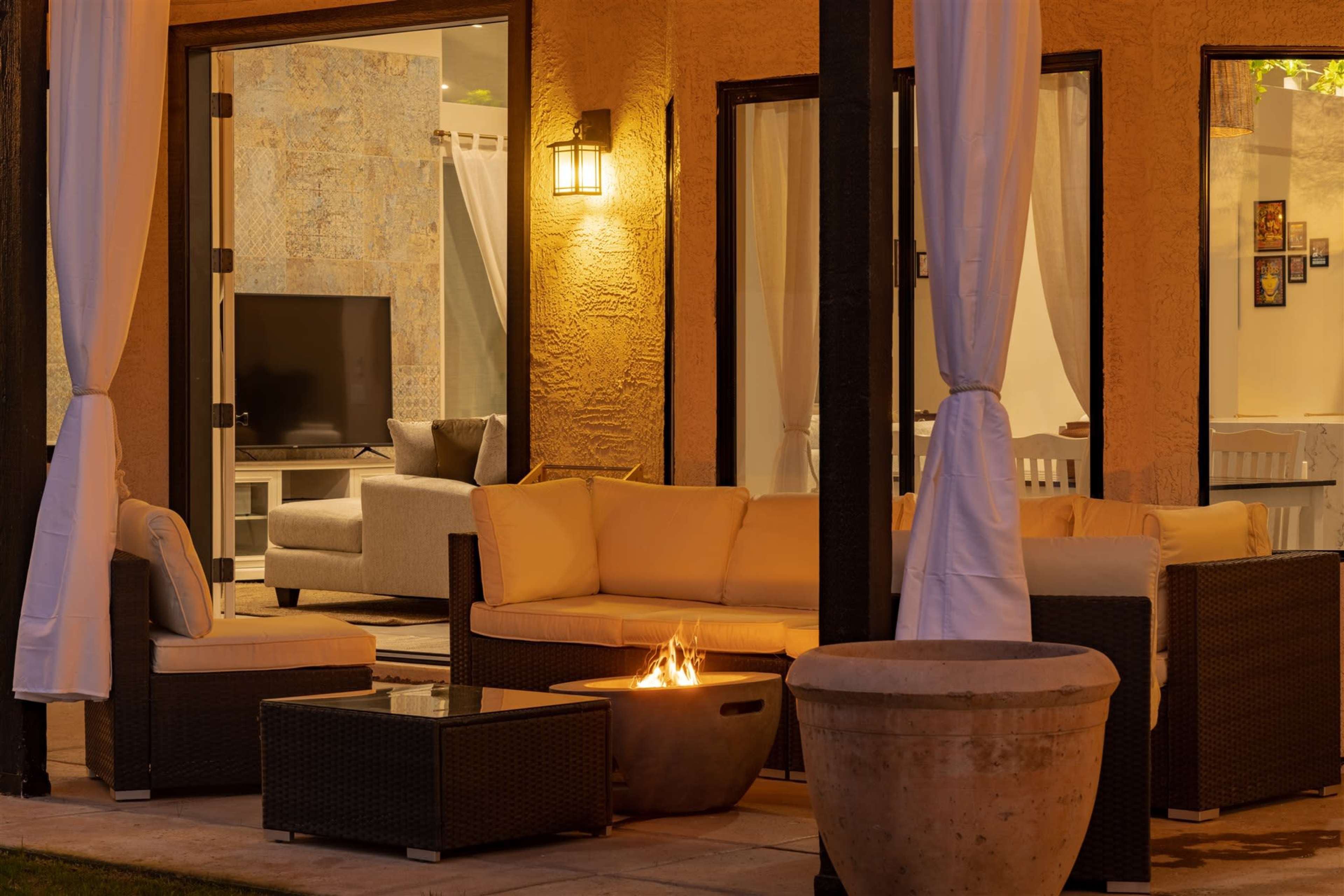A cozy outdoor seating area features a modern sofa set, a fire pit, and a view of a living room through an open sliding door.