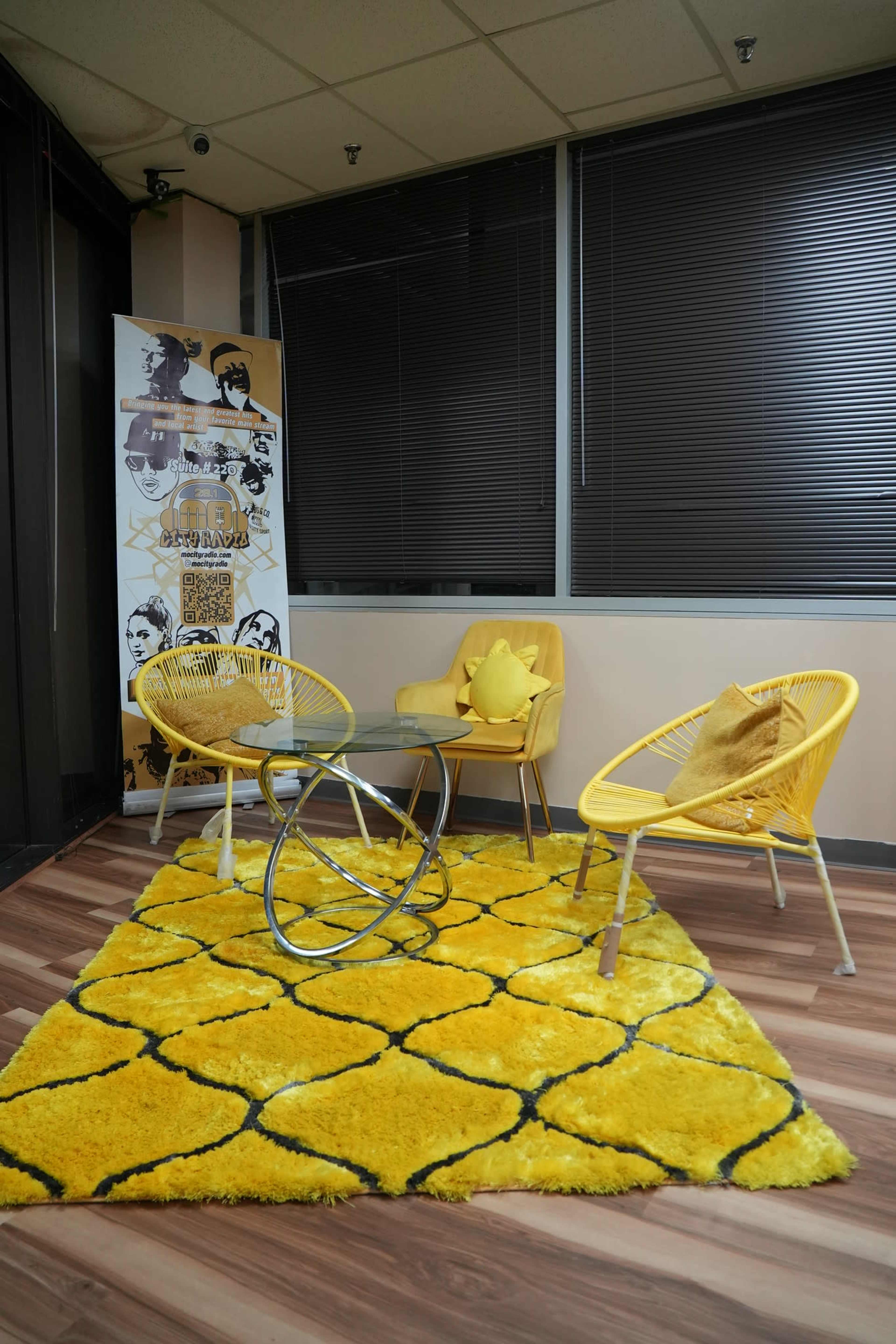 The image shows a modern seating area featuring three yellow chairs, a round coffee table, and a large yellow rug with a geometric pattern.