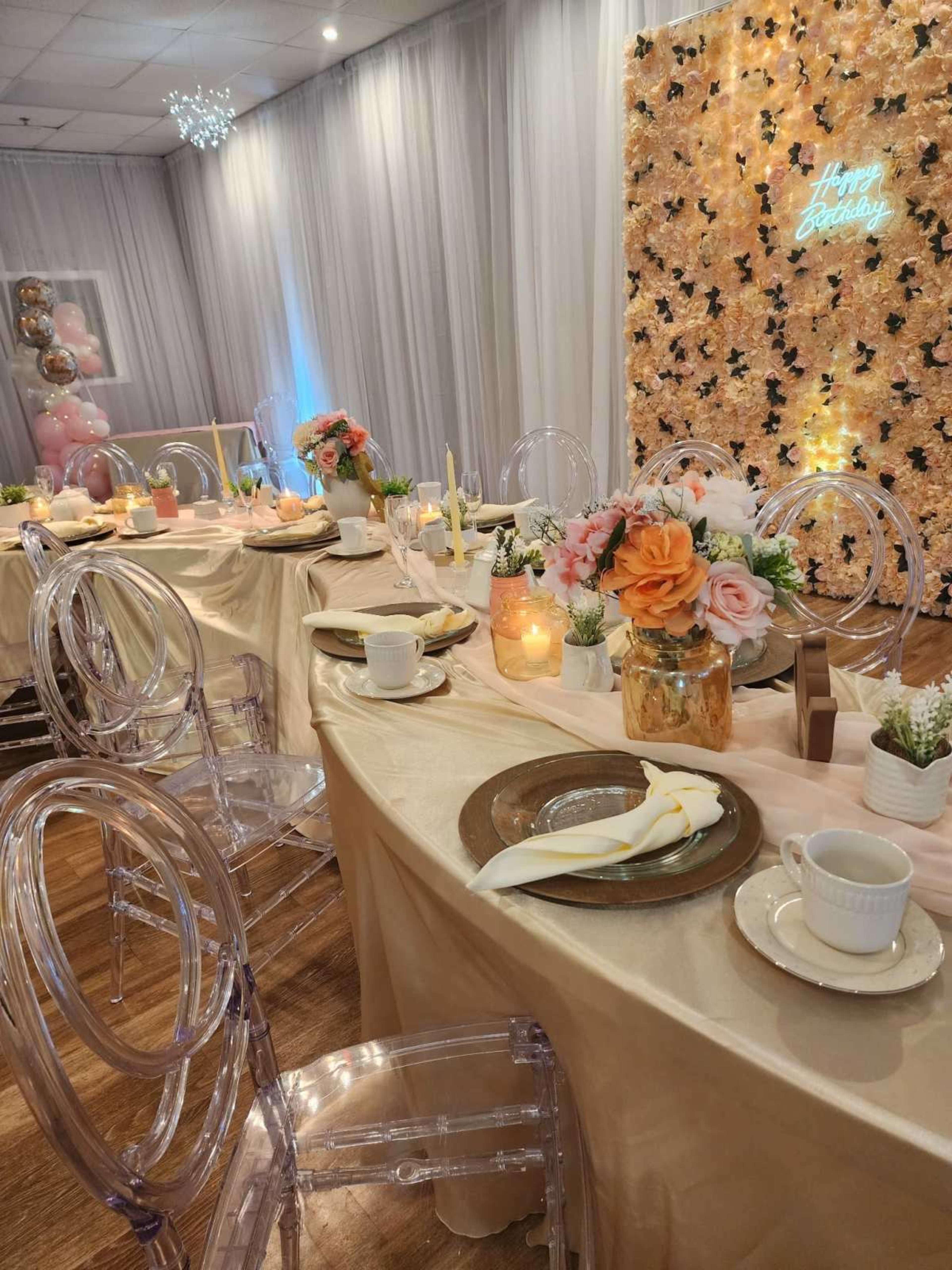 A decorated dining setup features elegant tables covered with gold tablecloths, adorned with flowers, candles, and place settings.