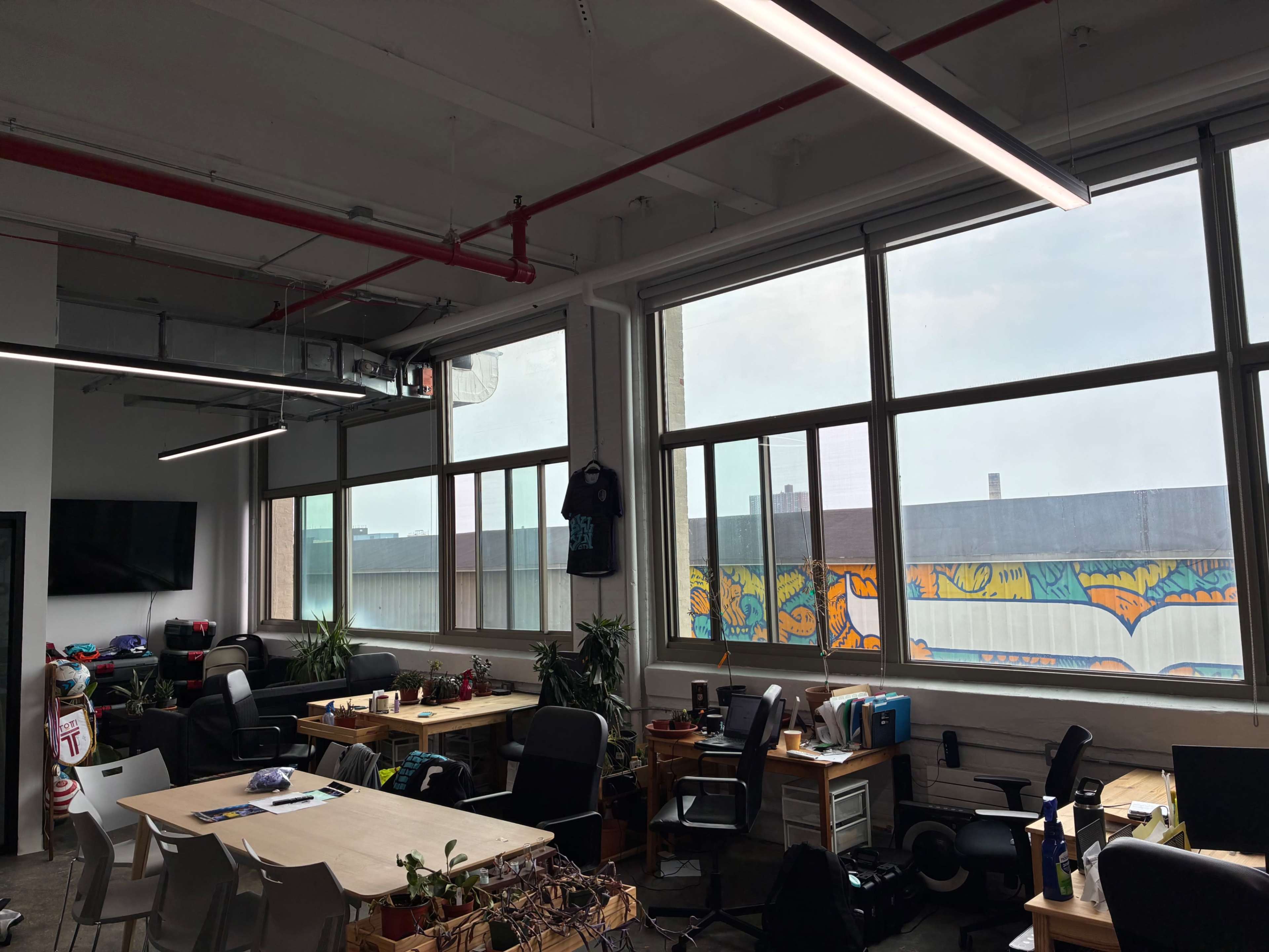 The image shows a modern office space with large windows, desks with chairs, and colorful graffiti visible on an outside wall.