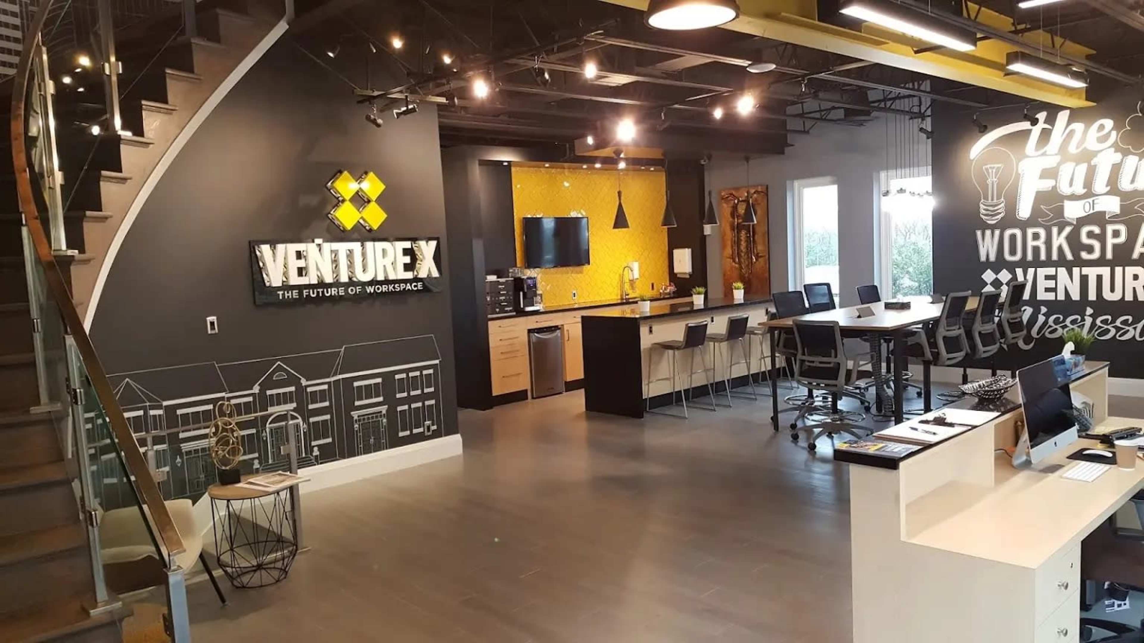 A modern office space featuring a reception area with a prominent "Venture X" sign, a kitchen counter, and various workstations.