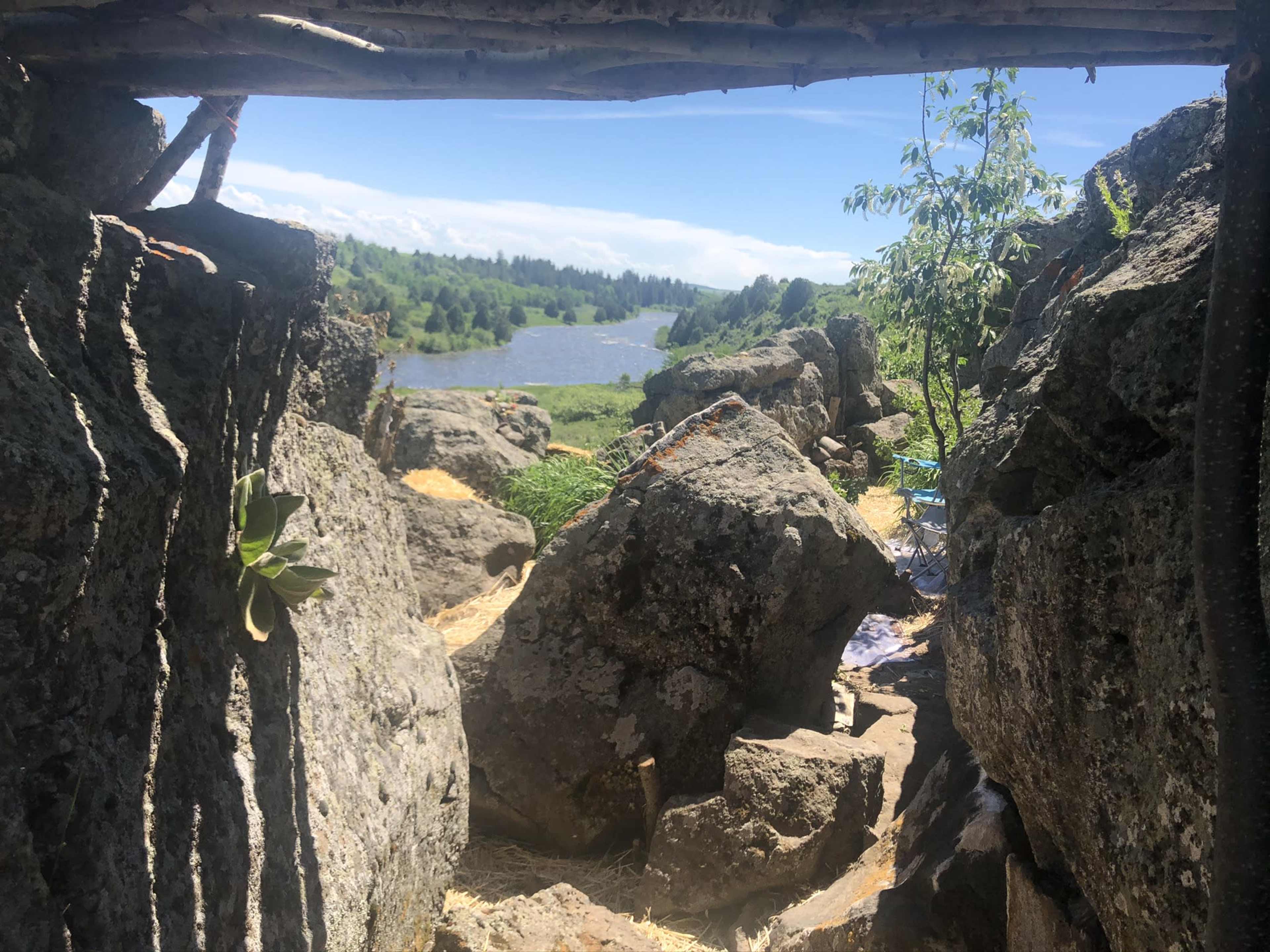 A view from a rocky shelter overlooking a river and green landscape under a clear sky.