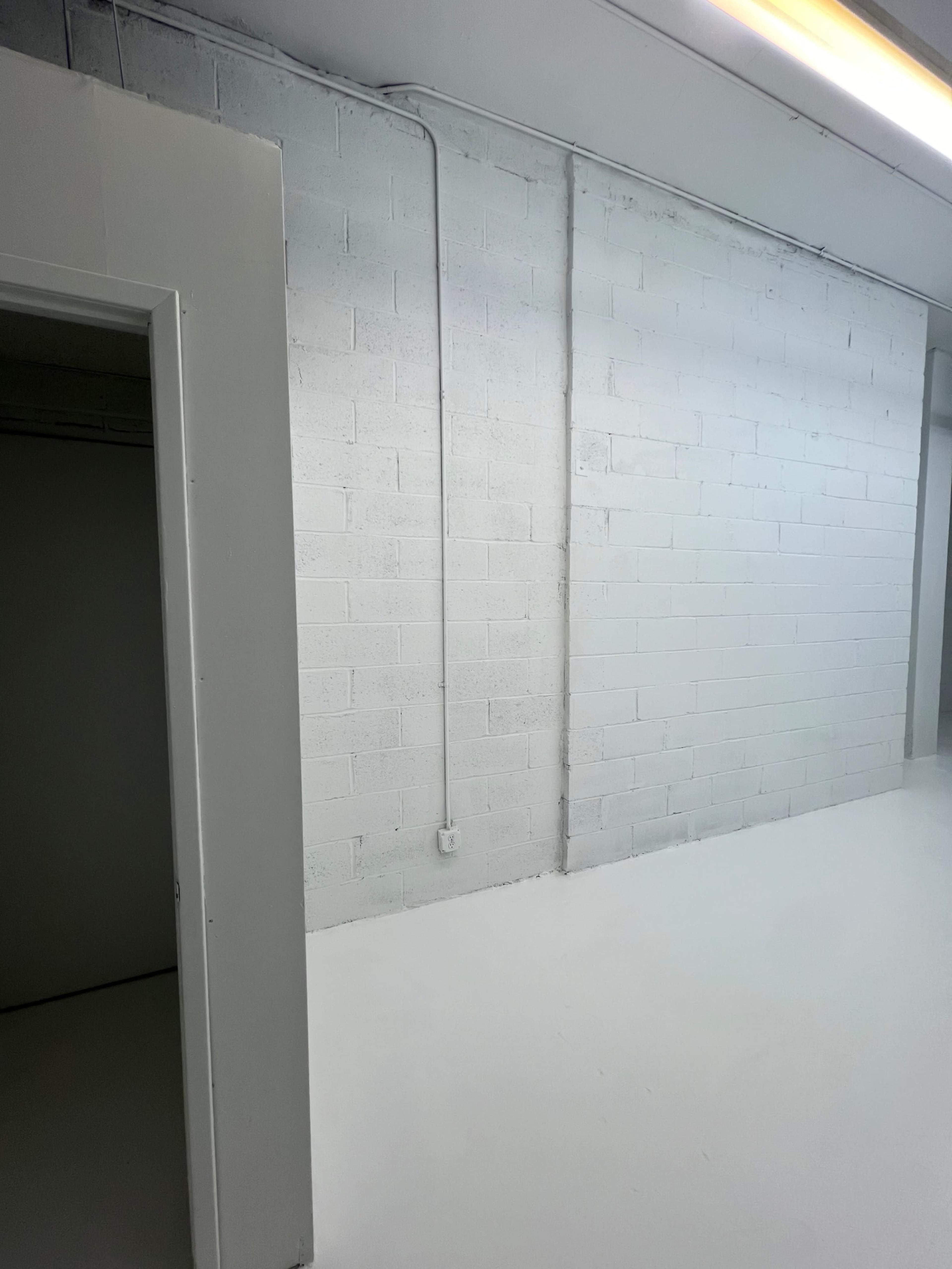 A spacious, empty room with white walls and a white floor, featuring an open doorway on the left.