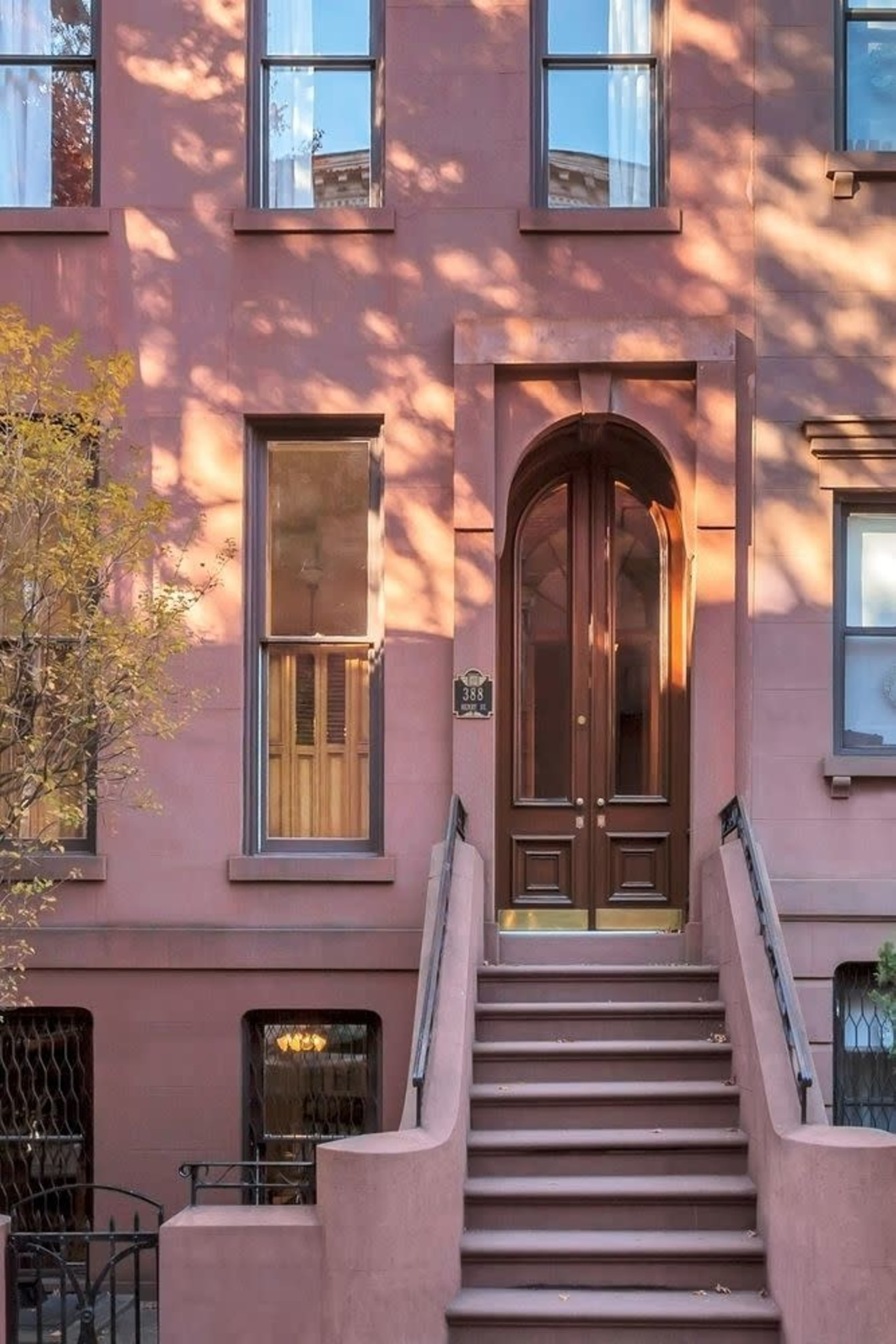 A brownstone building with a set of stairs leading up to a large arched wooden door framed by multiple windows.