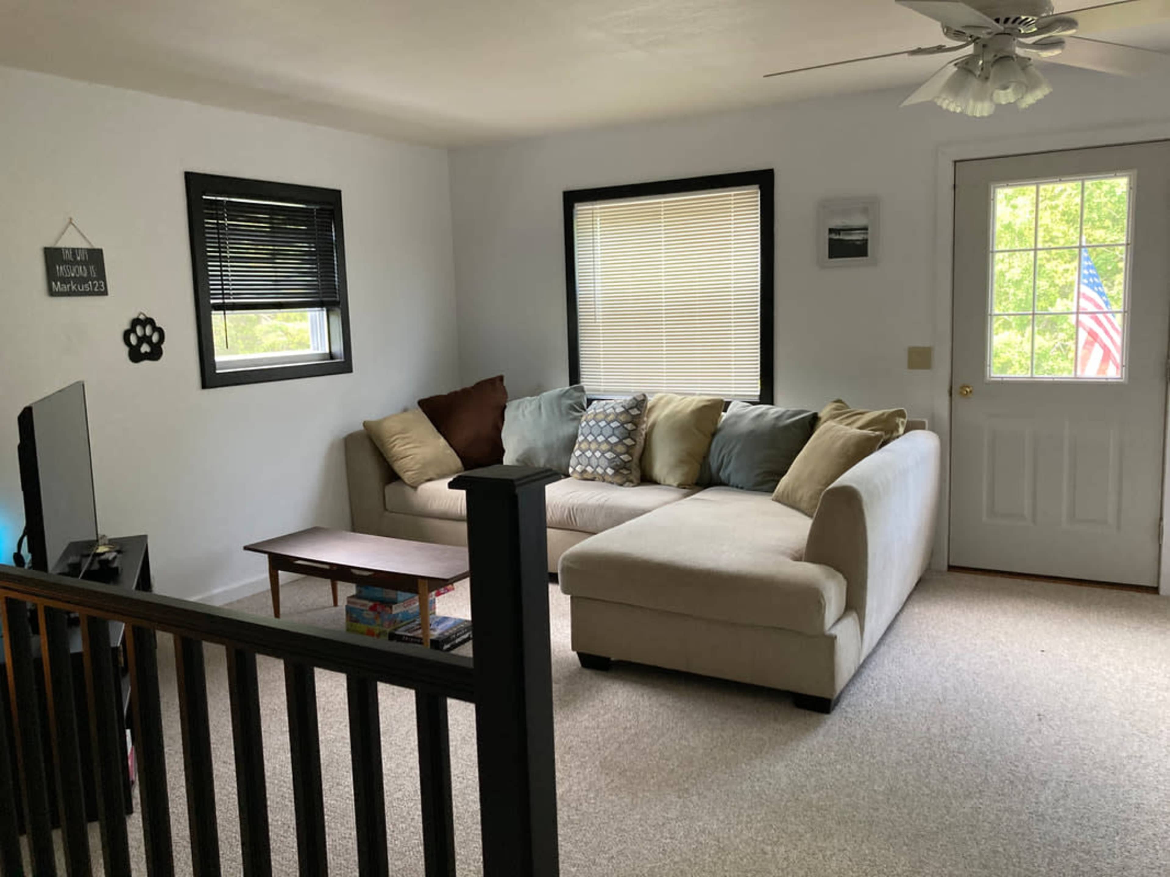 A living room with a sectional sofa, a small coffee table, a television, and a door leading outside, adorned with an American flag.