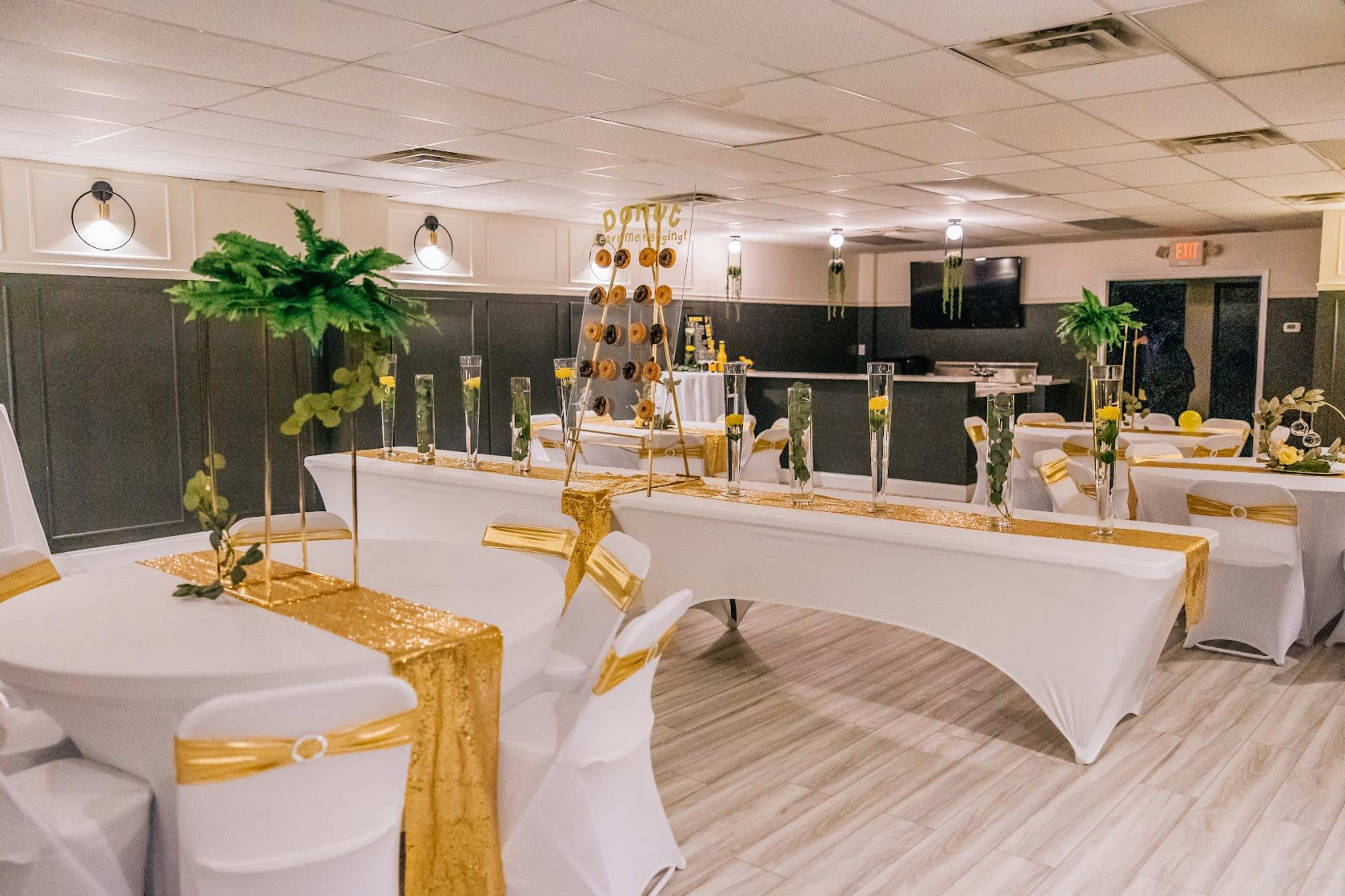 A banquet hall decorated with white and gold table settings, featuring long tables with glittering table runners and centerpieces.