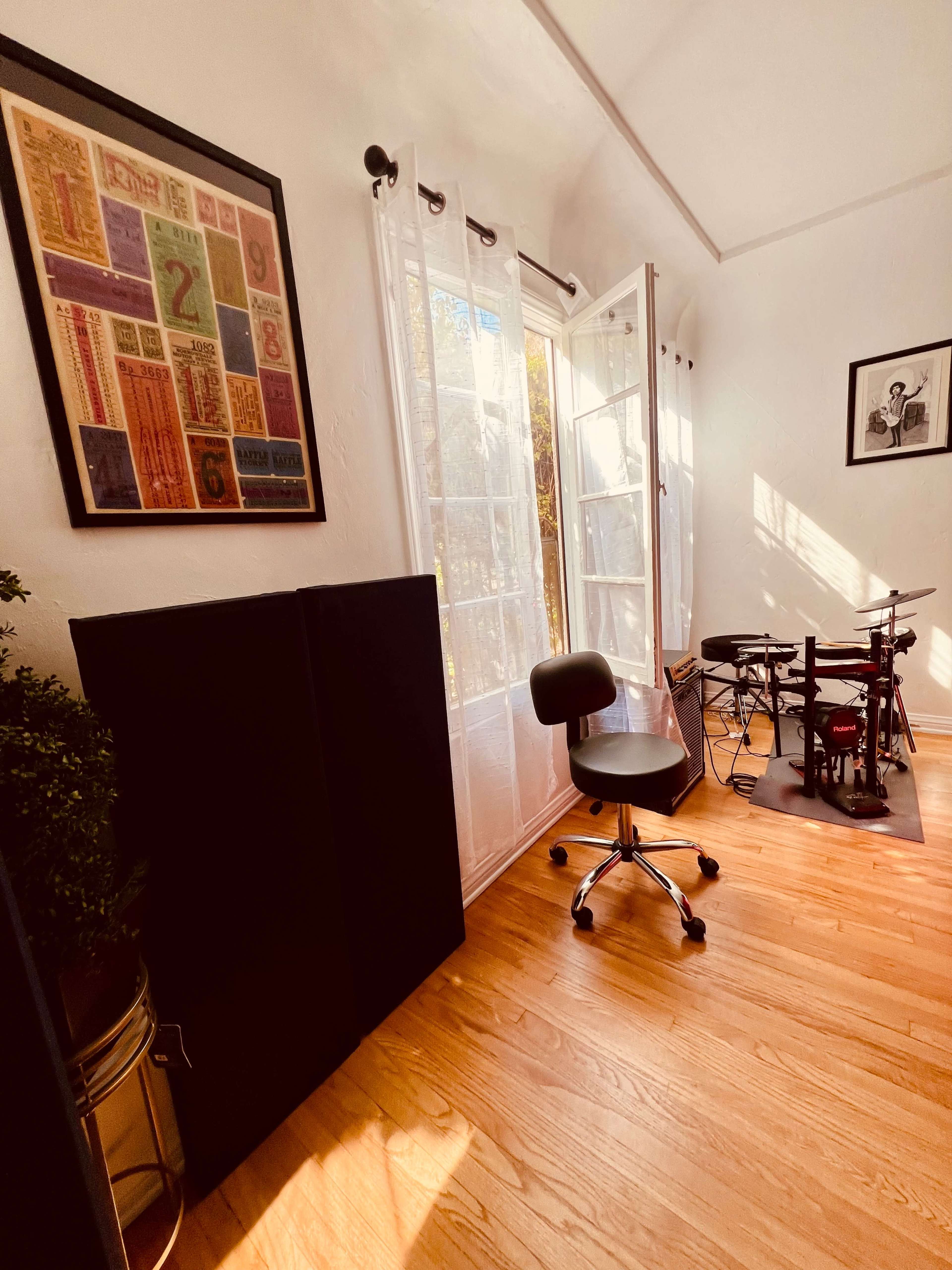 A well-lit room with a chair, a small electronic drum set, and a large window open to the outdoors.