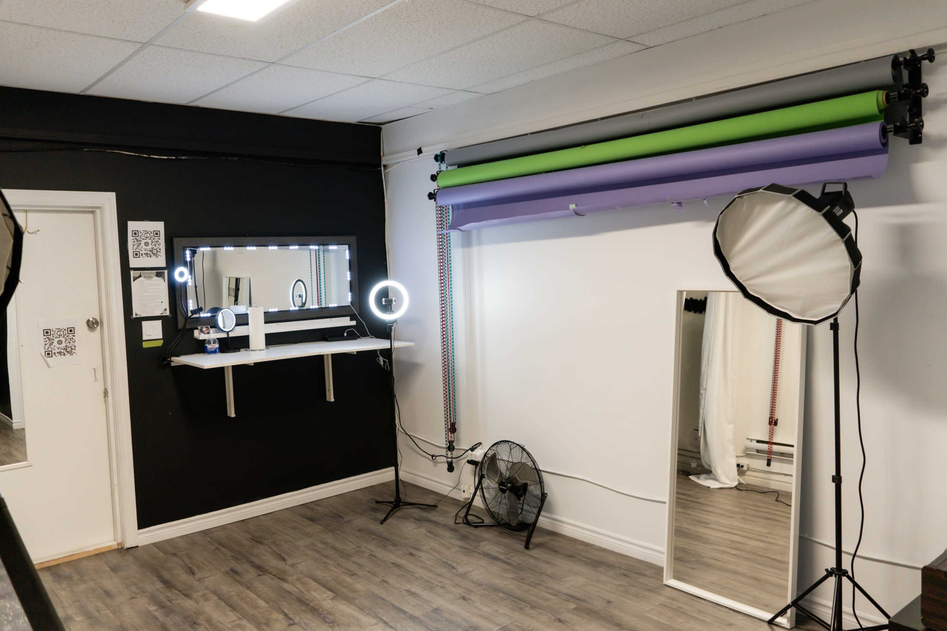 A photography studio featuring backdrops in green and purple, a mirror, softbox lights, and a circular light setup against a black wall.