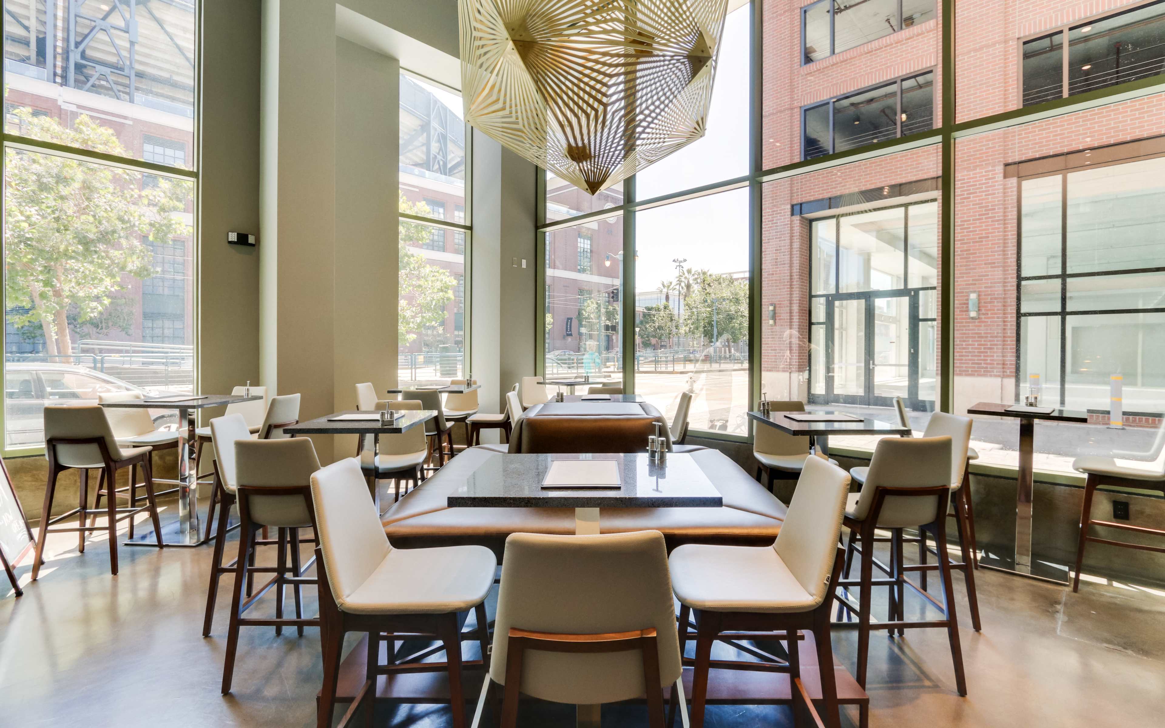 A modern restaurant interior with large windows, featuring several tables and chairs arranged around the space.