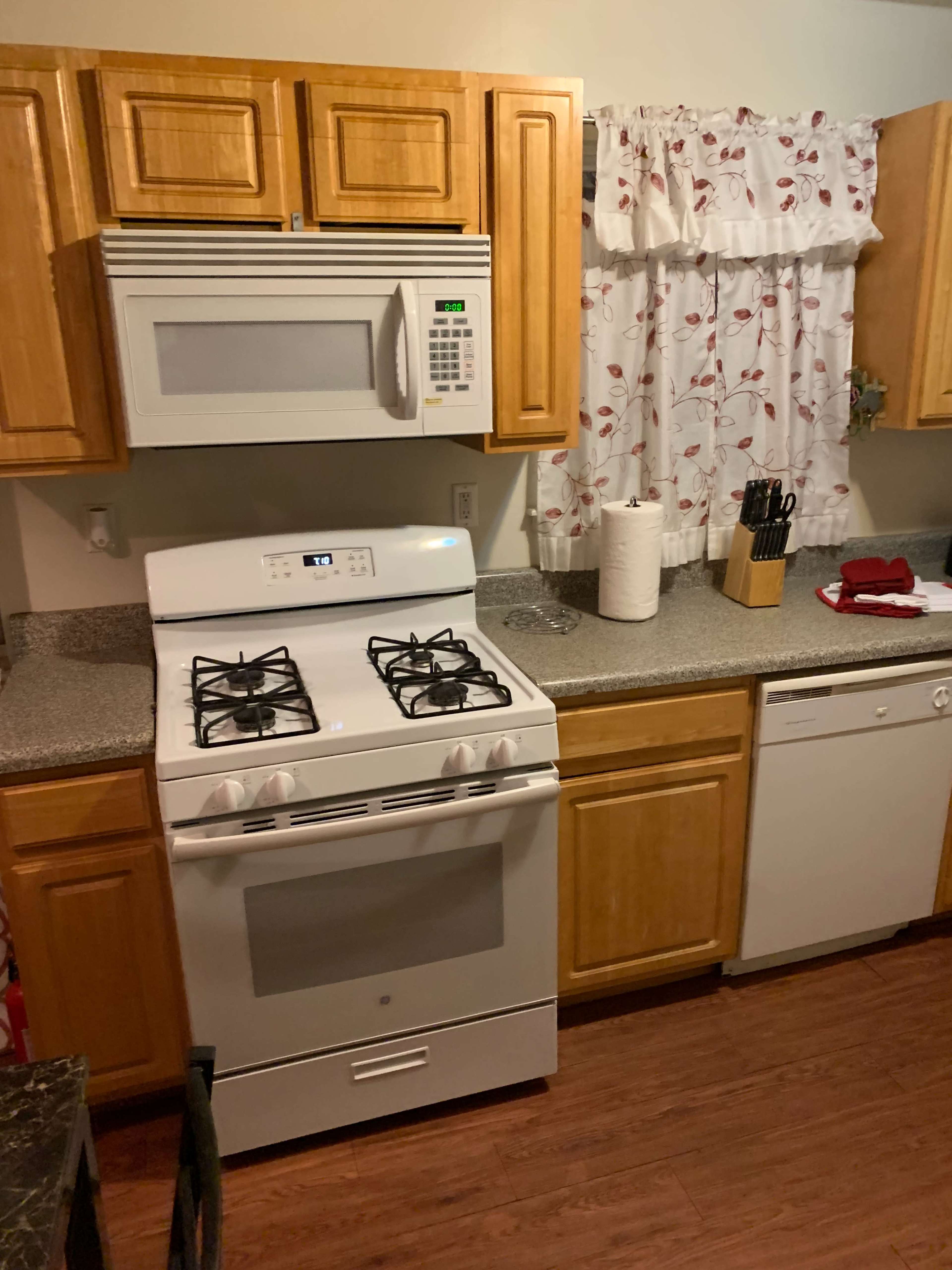 A kitchen with wooden cabinets, a gas stove, a microwave above it, a countertop with kitchen utensils, and a dishwasher beside the stove.