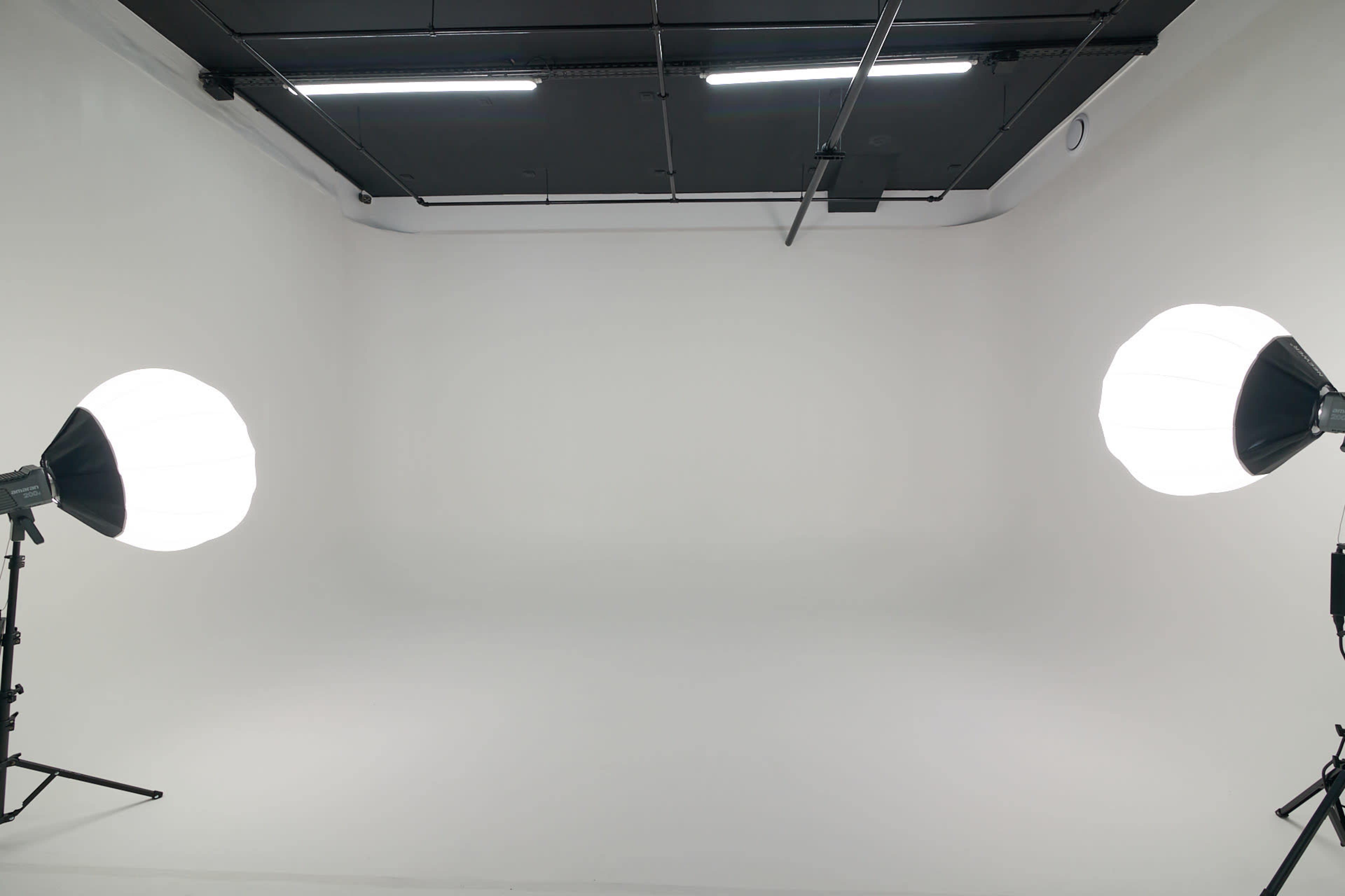 The image shows a spacious studio with a white backdrop and two softbox lights positioned on either side.