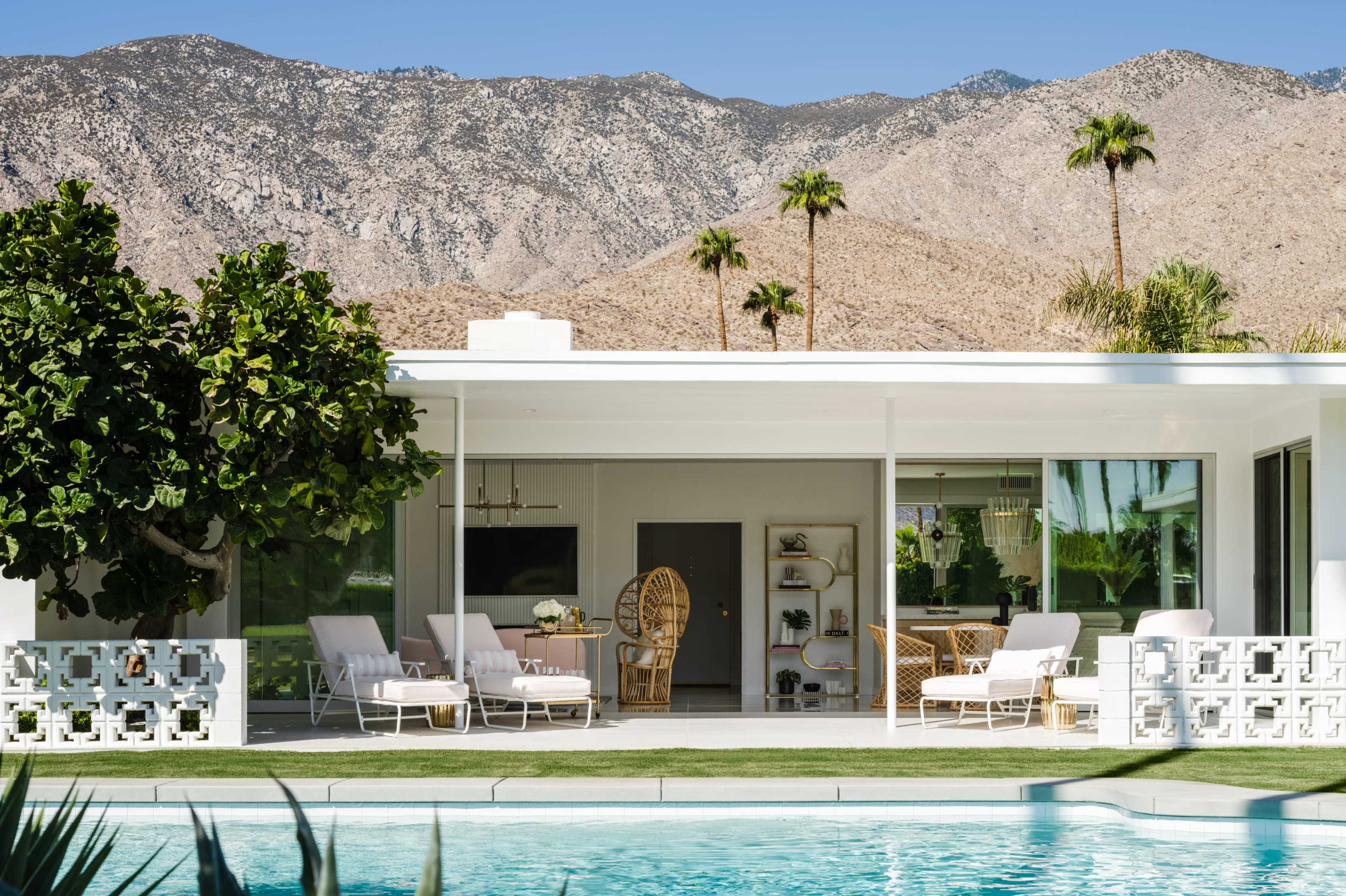 A modern house with a swimming pool features a patio with lounge chairs and views of a mountain landscape in the background.