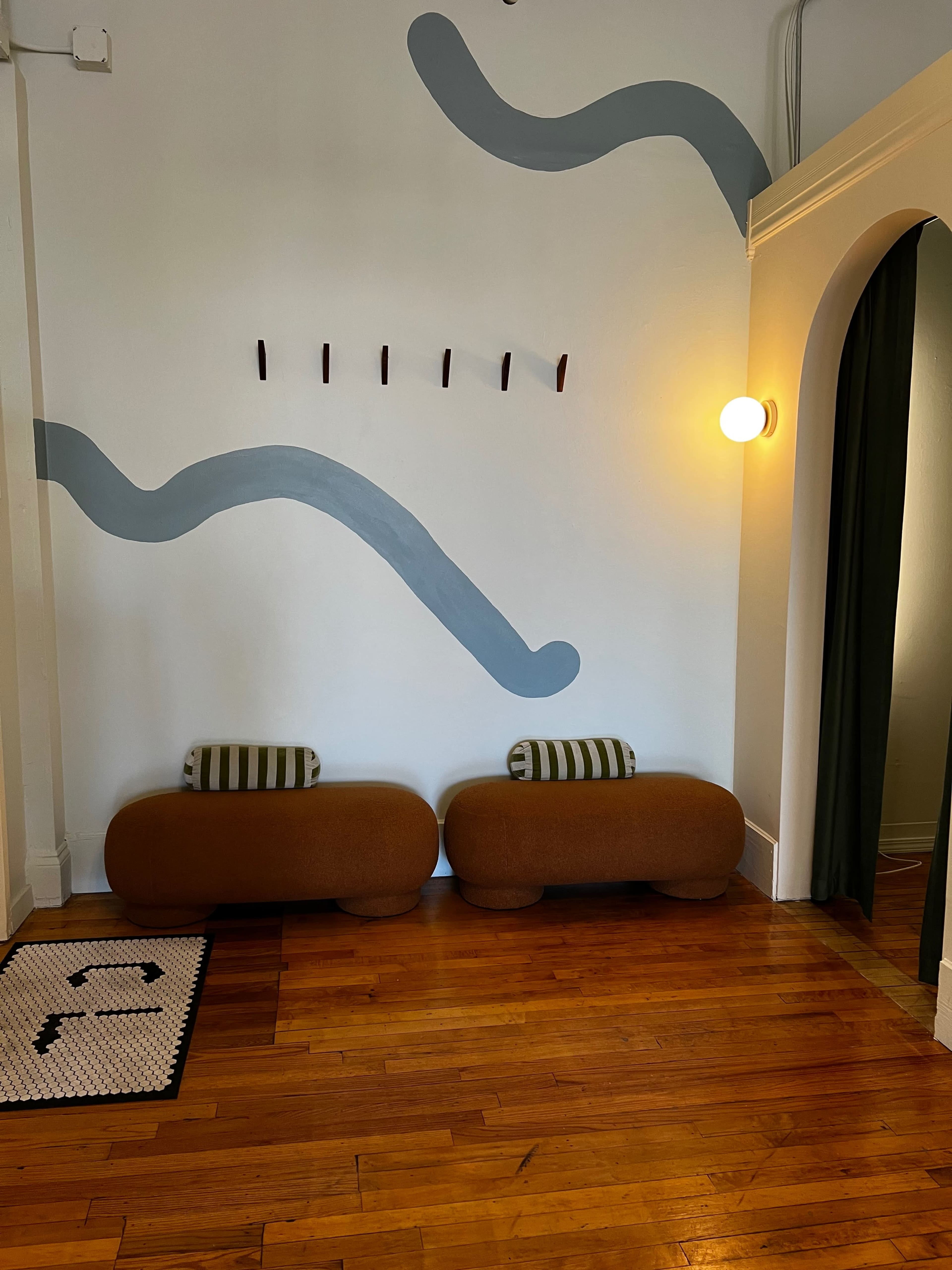 The image shows a cozy interior space featuring two rounded brown benches with striped cushions, a light fixture, and decorative blue wall patterns.