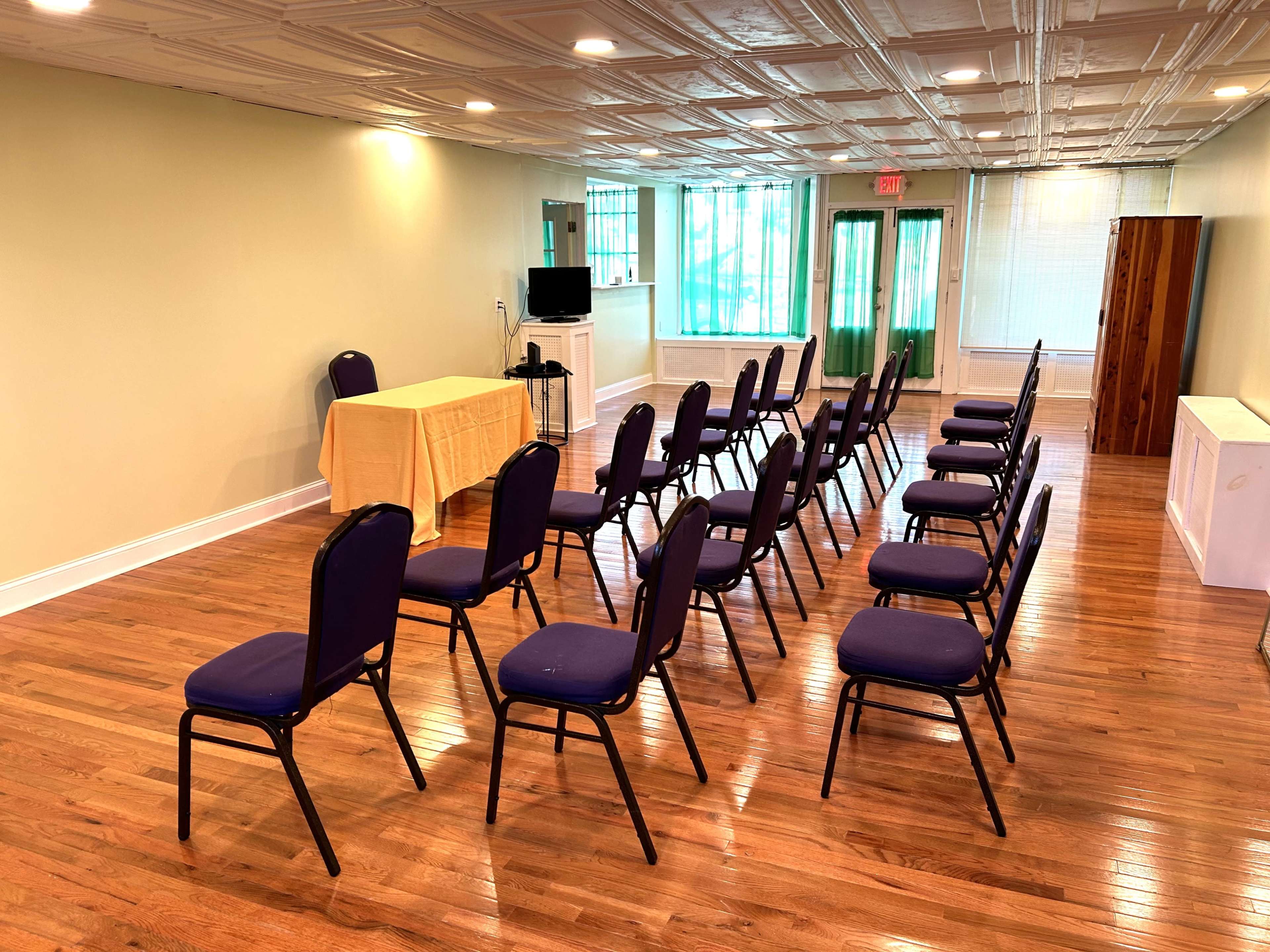 A meeting room is set up with rows of purple chairs facing a table covered with a yellow cloth.