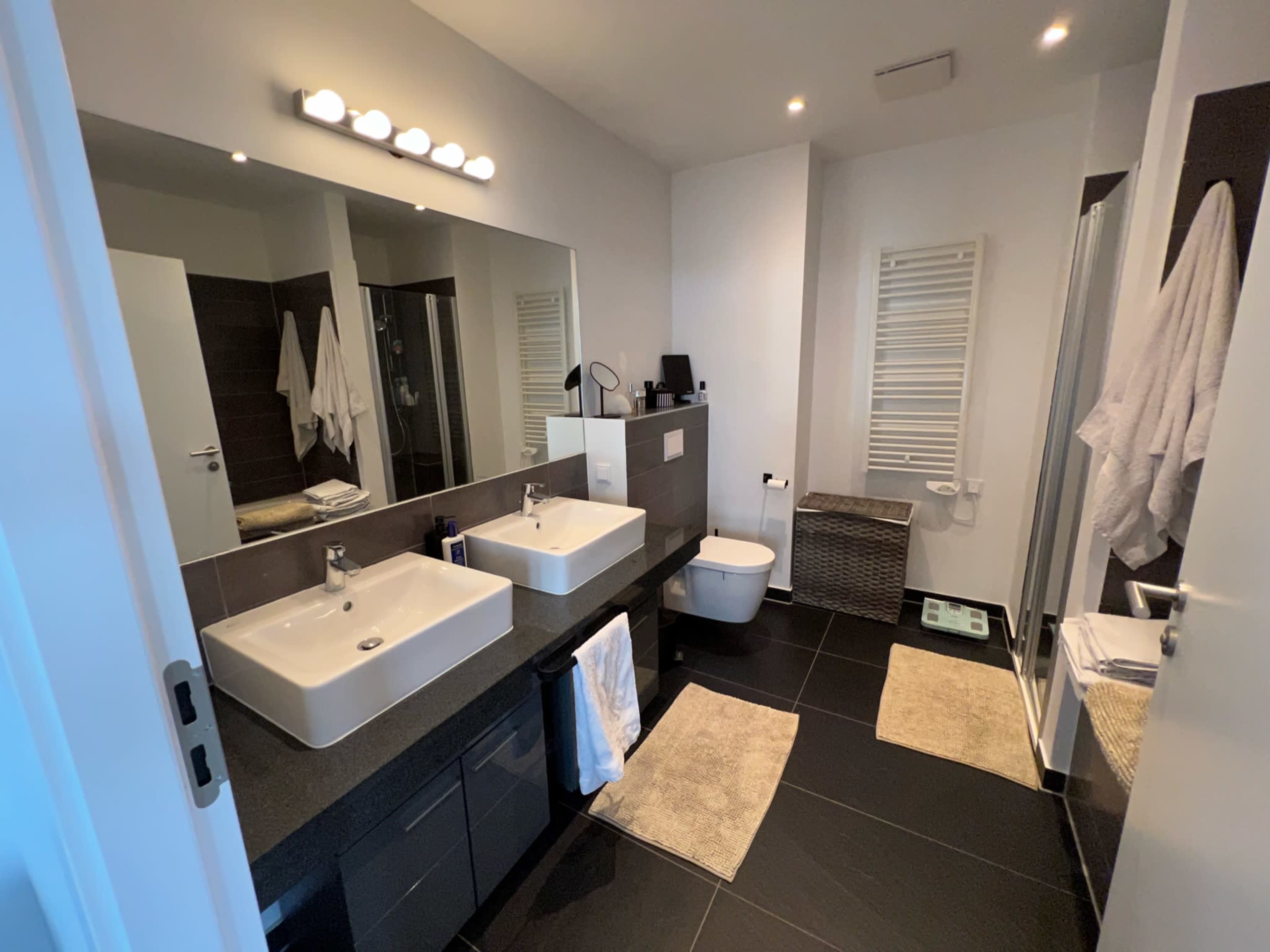 A modern bathroom featuring double sinks, a walk-in shower, and a towel rack, with gray and white decor.