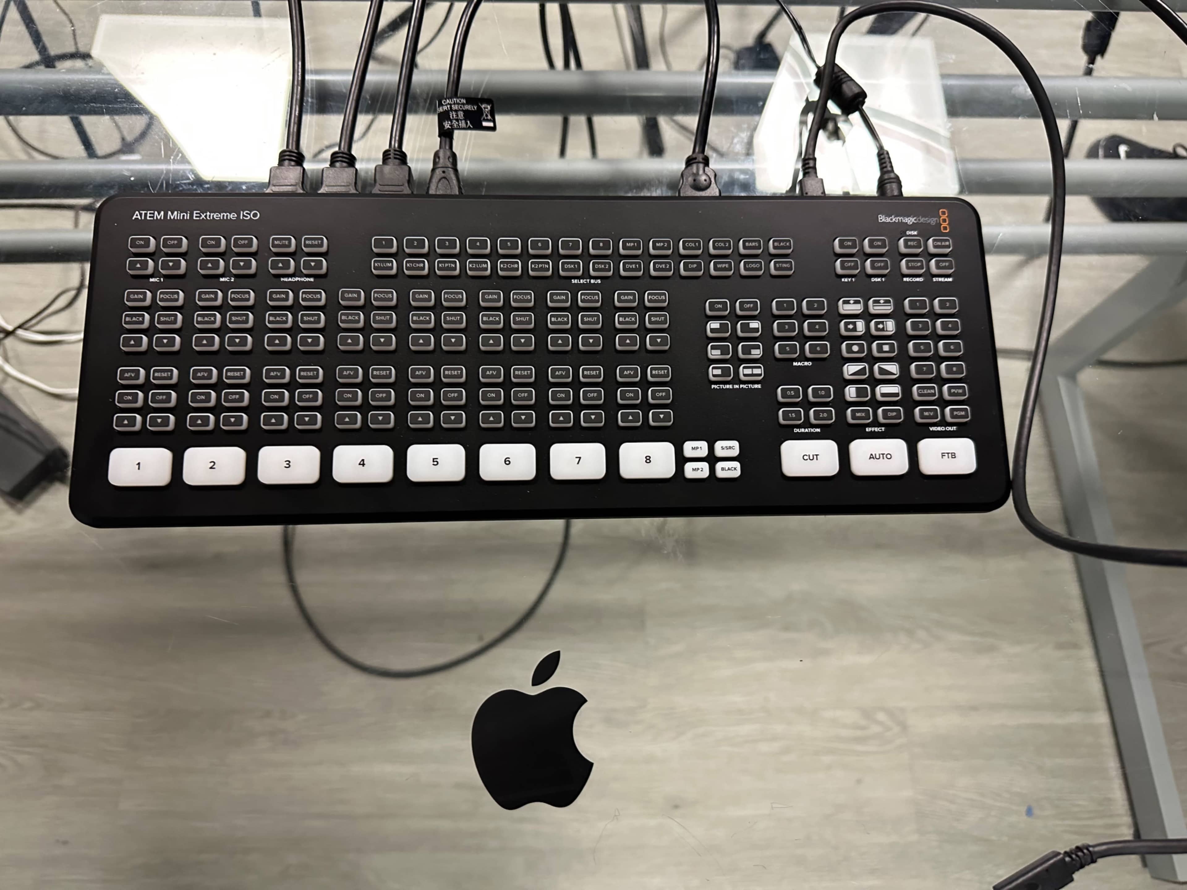 A Blackmagic ATEM Mini Extreme ISO control panel positioned on a glass surface with an Apple logo beneath it.