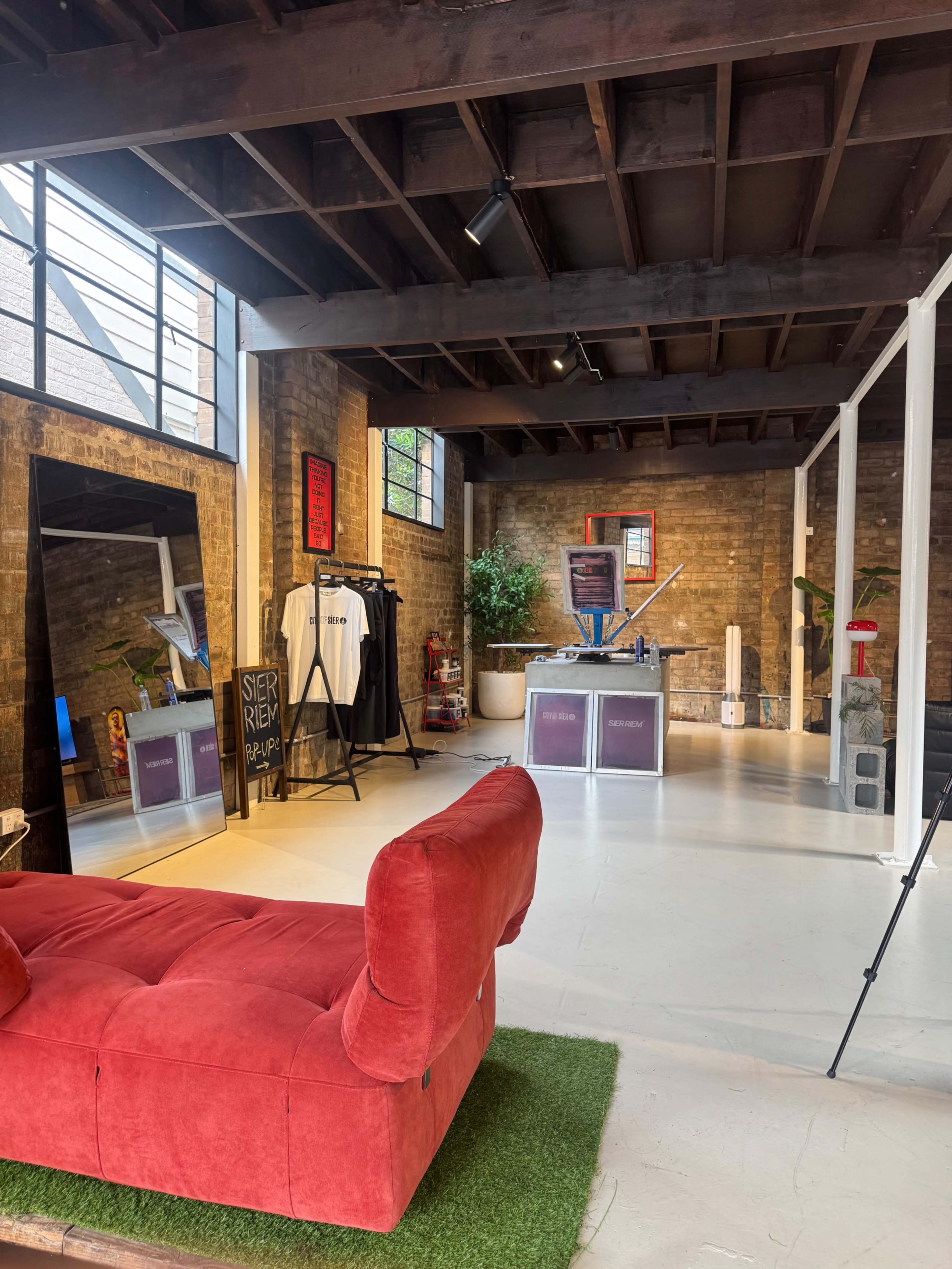 The interior of a modern studio space features a red couch, a large mirror, shelving units, and a mix of plants and art on the walls.