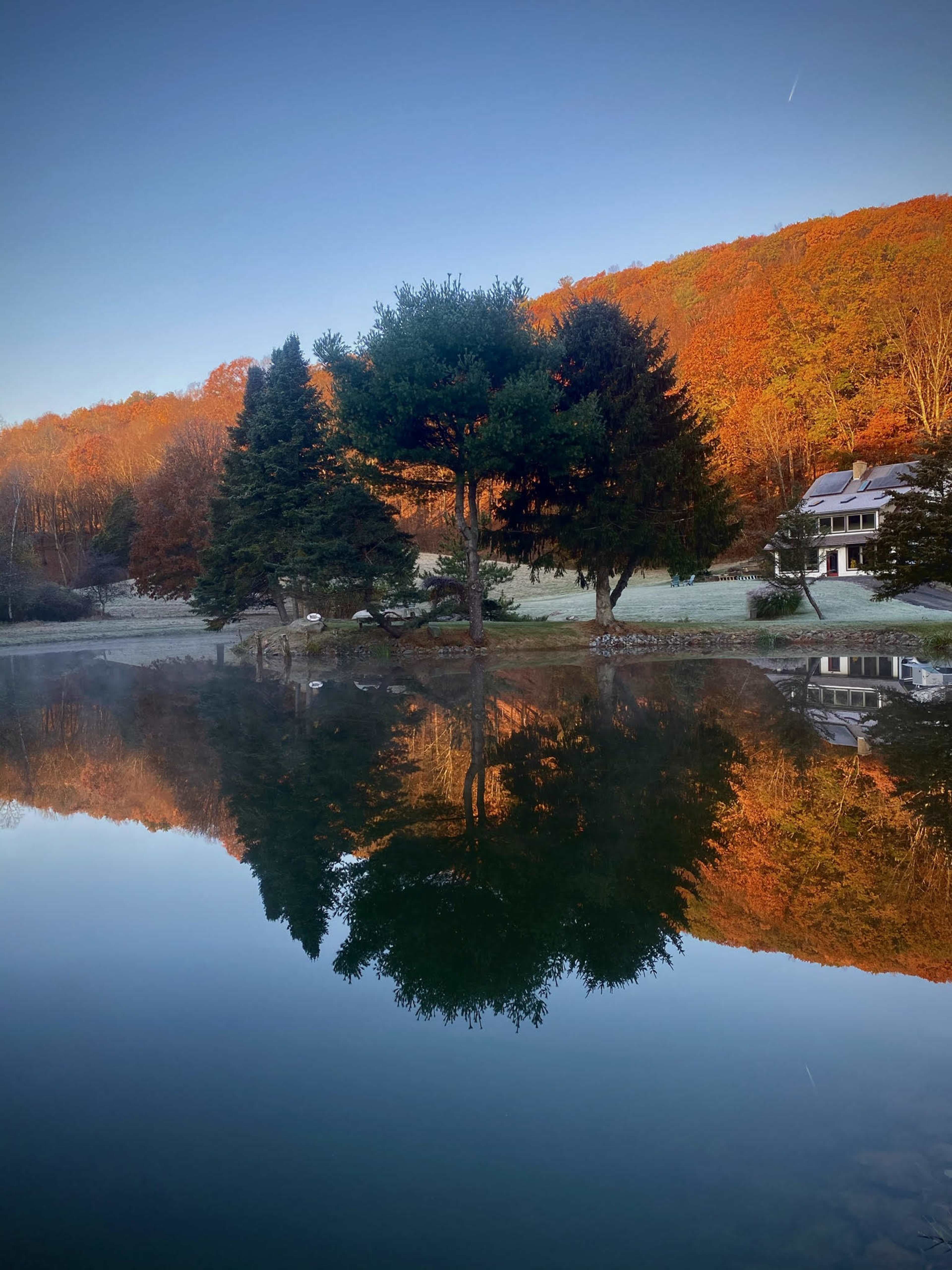 A serene lake reflecting colorful autumn trees and a house surrounded by a hillside.