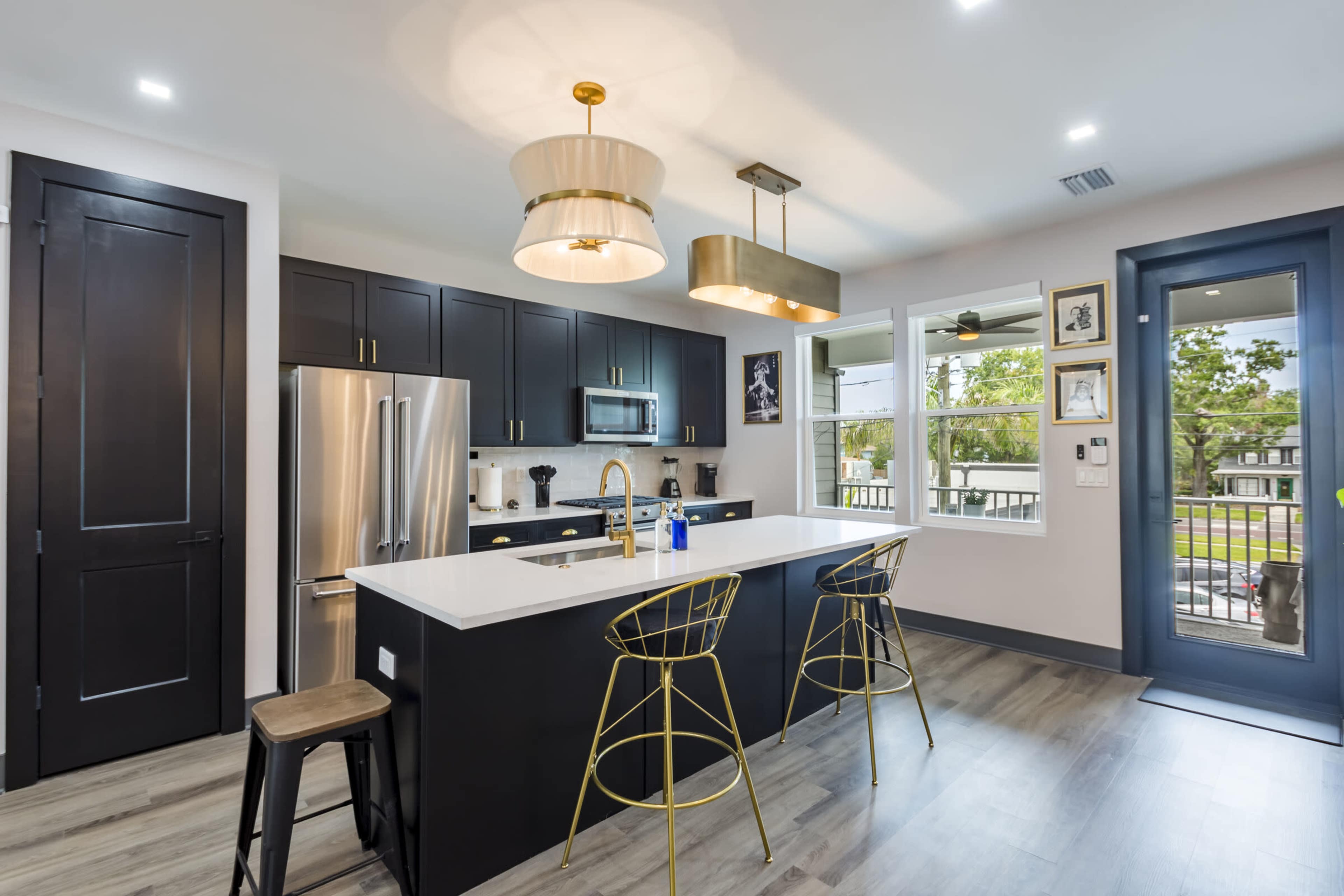 The image shows a modern kitchen with black cabinetry, a white countertop, and two gold bar stools at a central island.