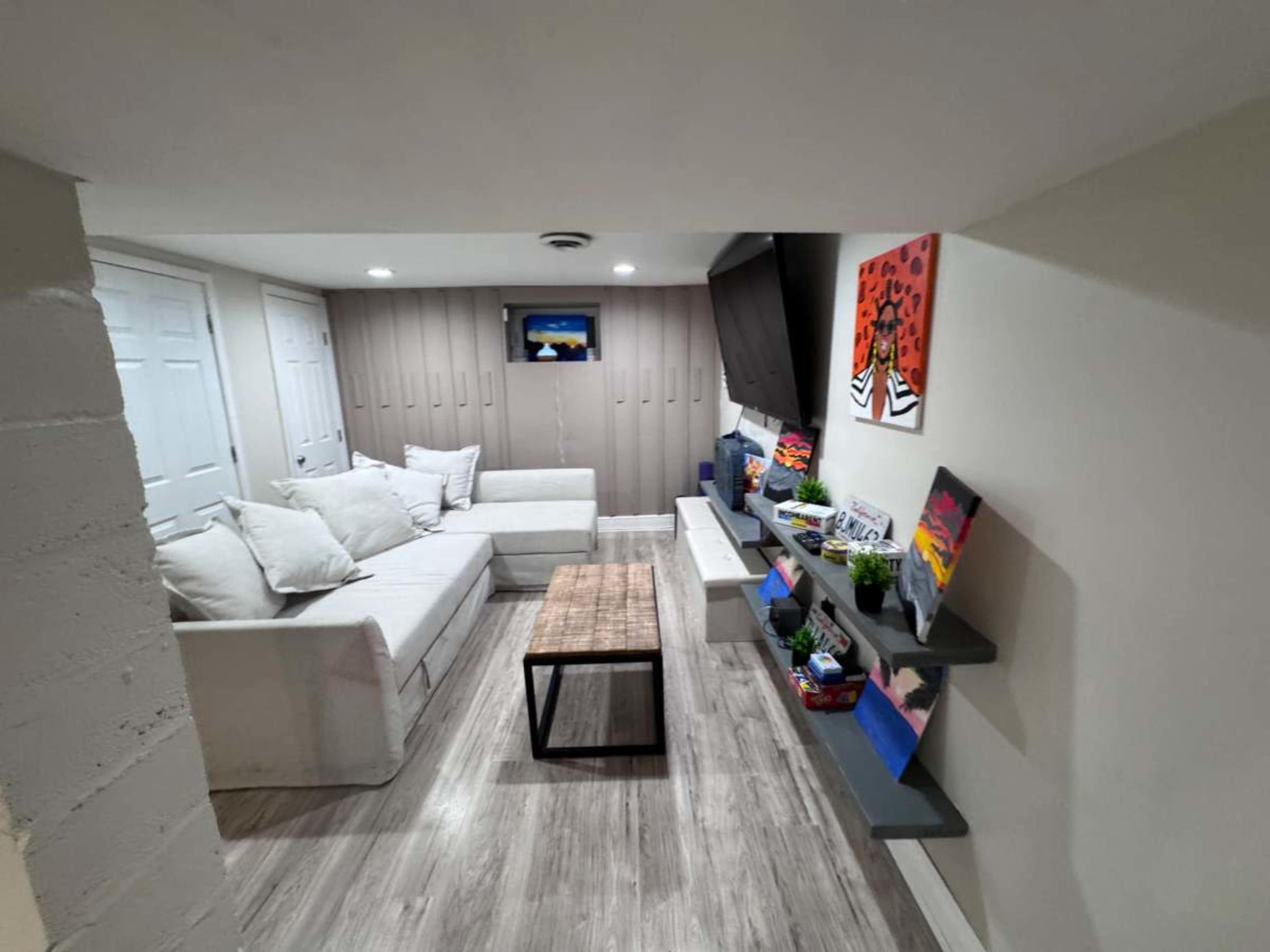 The image shows a modern basement lounge area with a sectional sofa, a wooden coffee table, and a wall-mounted television.