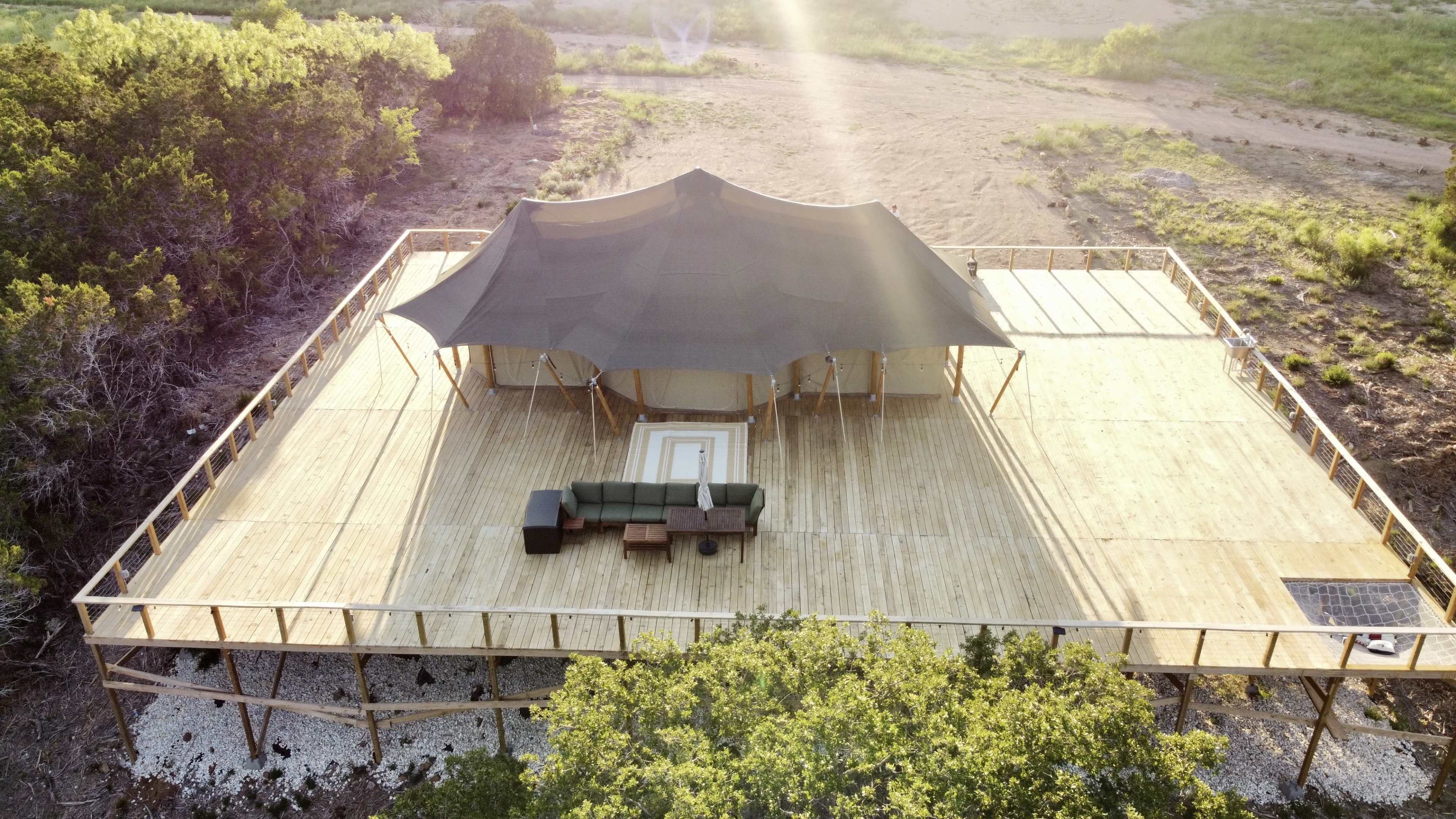 A large wooden deck features a tent structure with a seating area and is surrounded by a natural landscape.