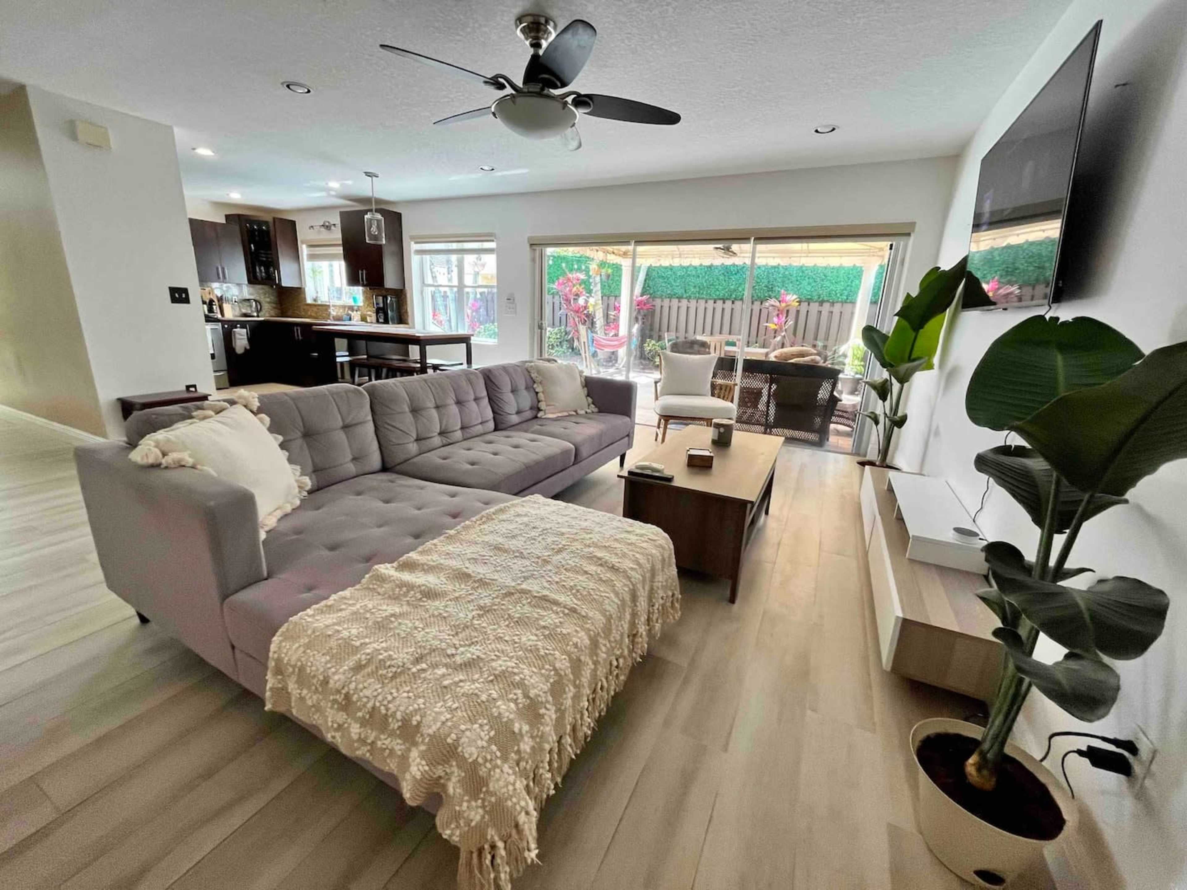 The image shows a living room with a gray sectional sofa, a wooden coffee table, and a large window overlooking a patio area.