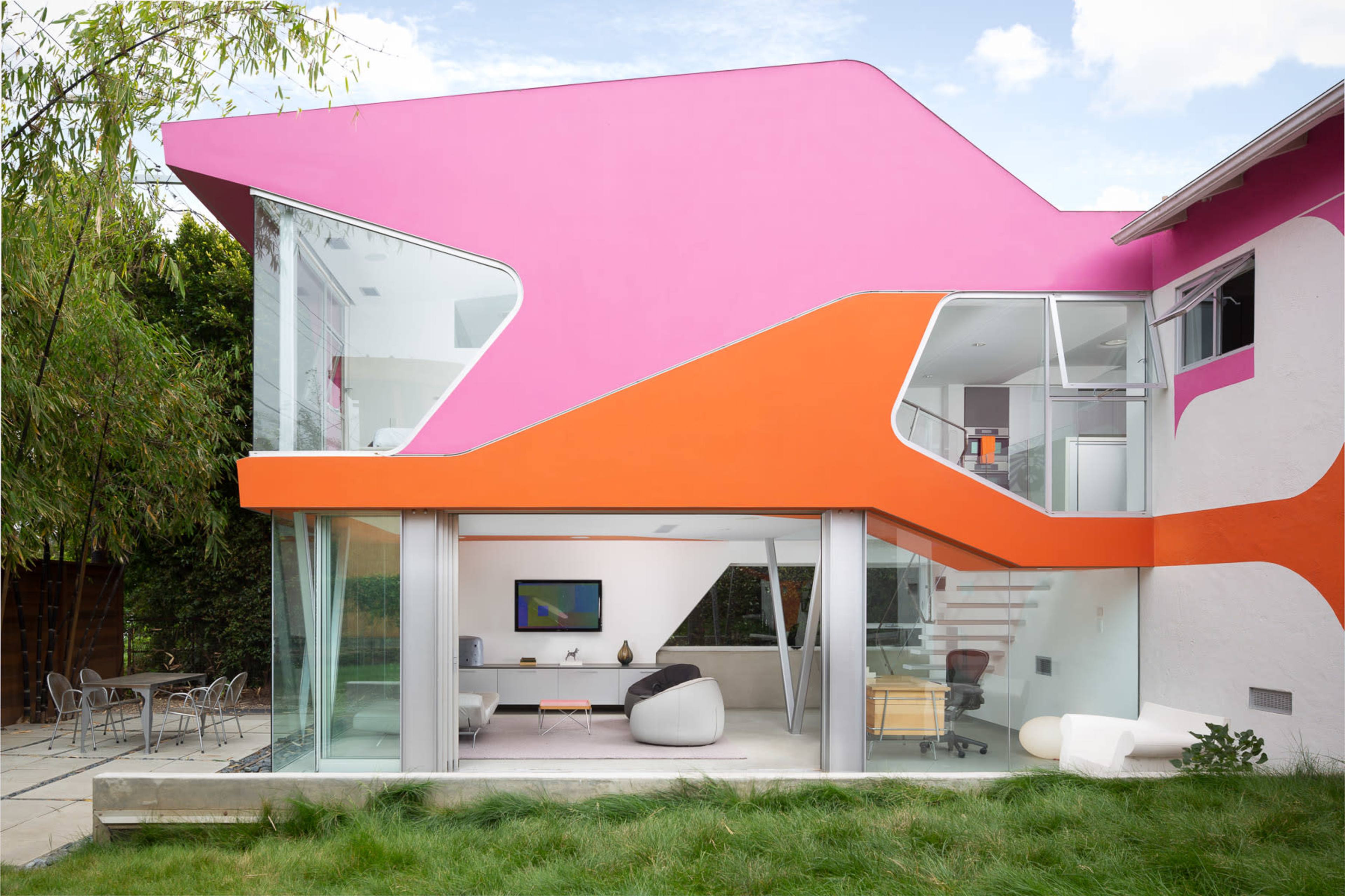 A modern house with vibrant pink and orange geometric designs on the exterior, large glass windows, and a landscaped backyard.