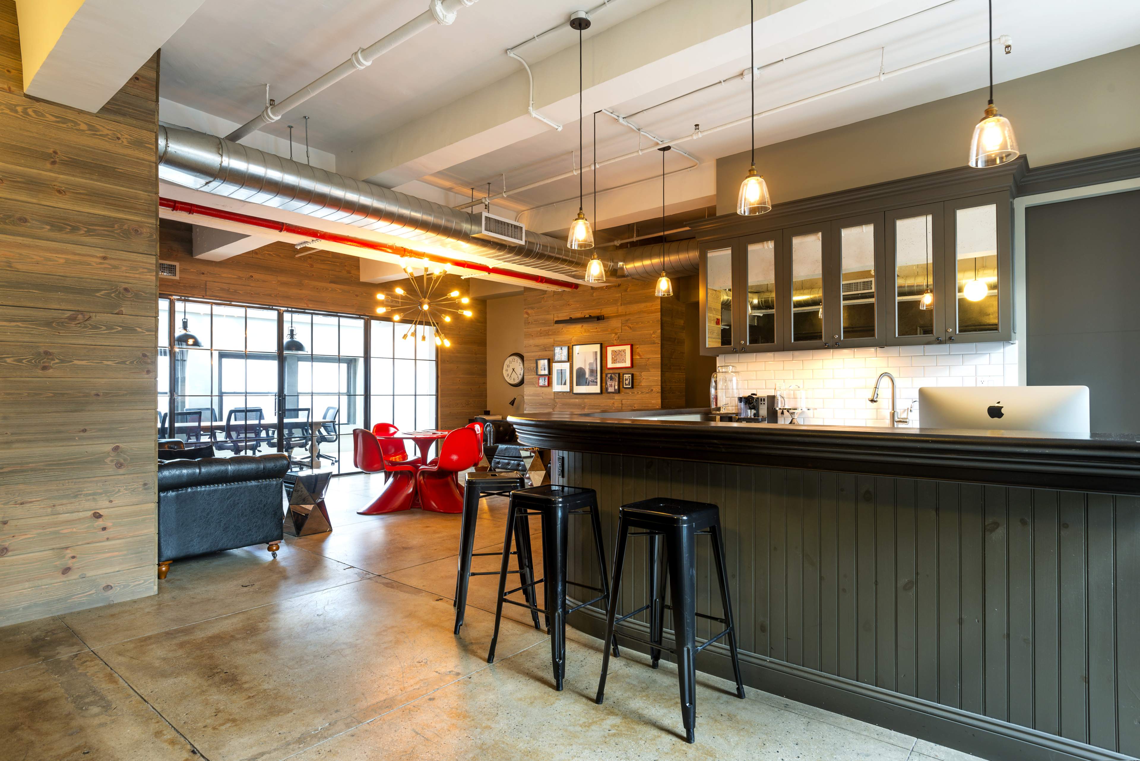 A modern open-concept kitchen and dining area features a bar with black stools, a red dining table, and various framed artworks on the walls.
