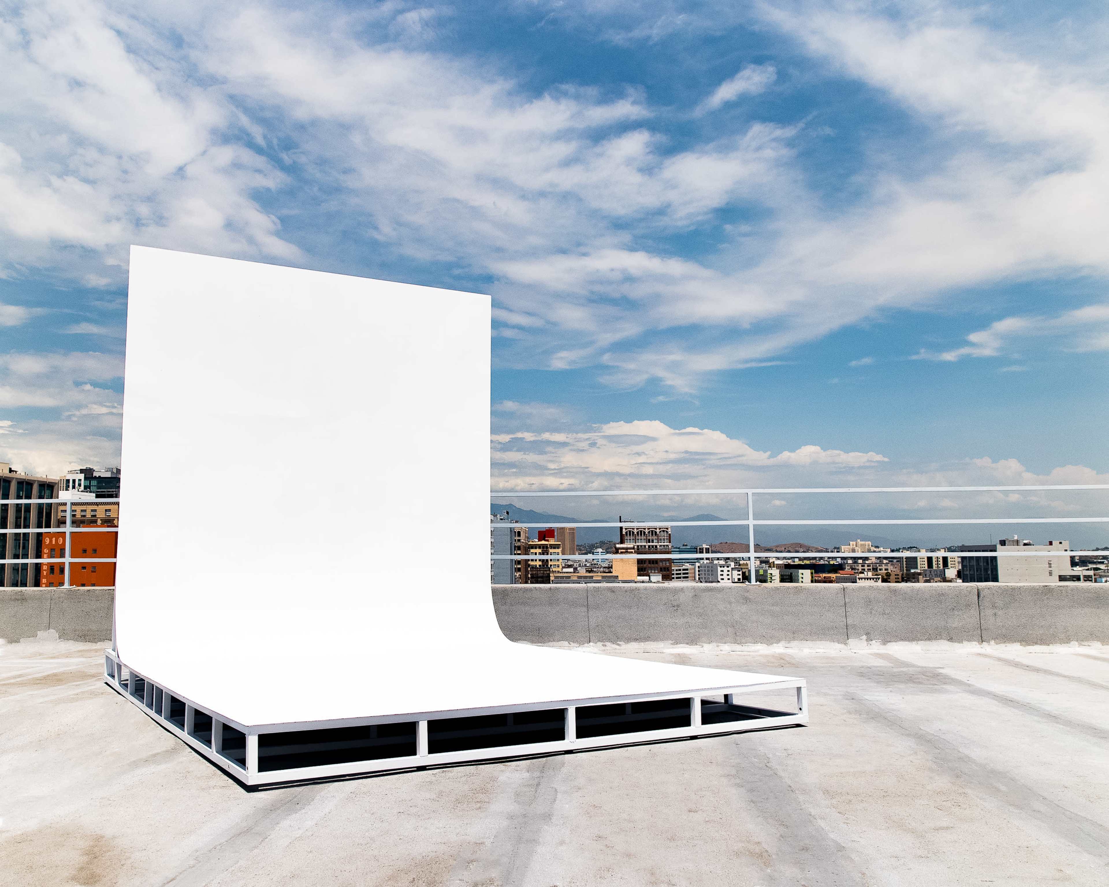 A large, white, curved display structure is positioned on a rooftop with a city skyline and blue sky in the background.